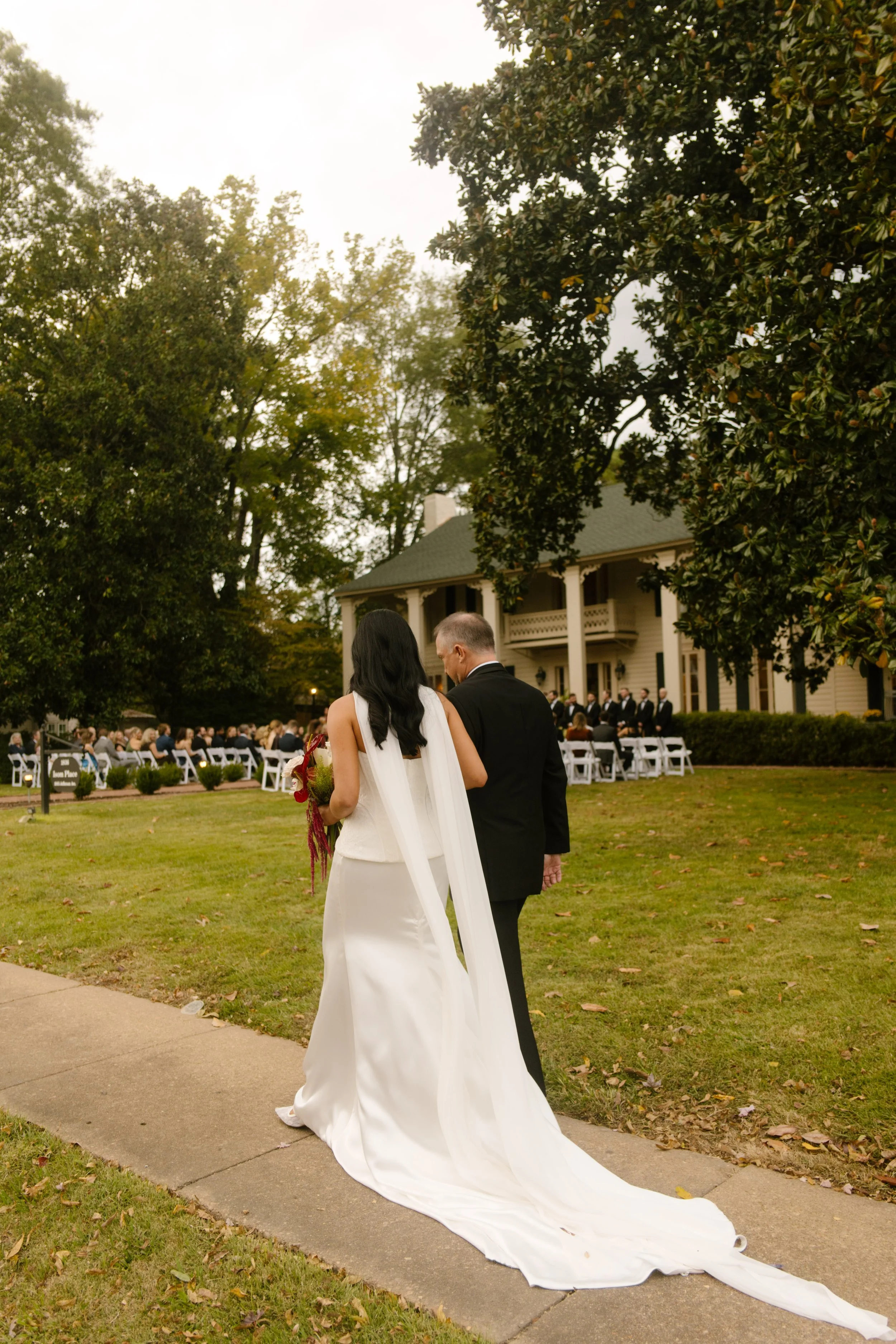 Bride and groom walking toward their outdoor wedding ceremony, with the bride's long white train flowing behind her.