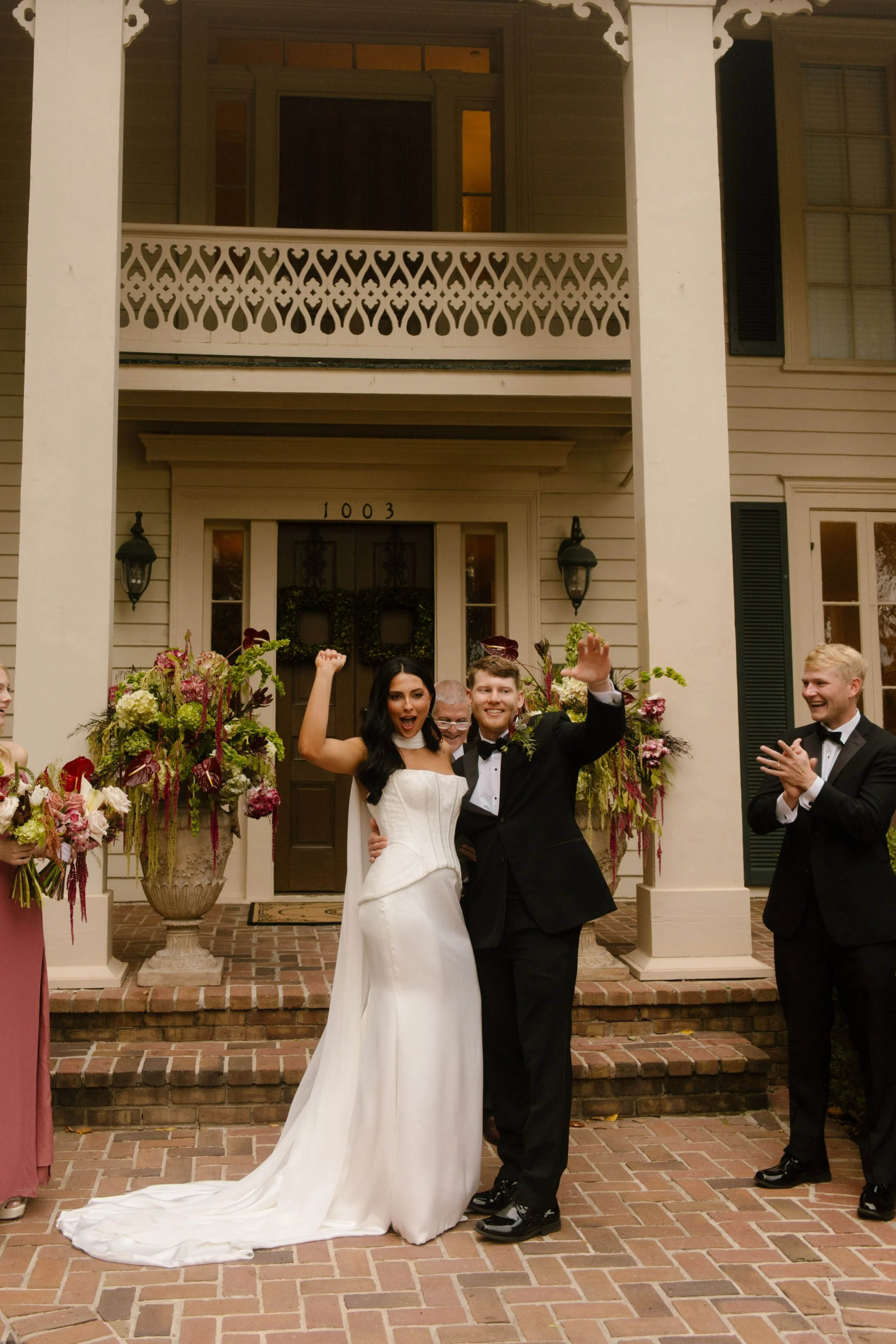 Bride and groom celebrating outside a historic wedding venue surrounded by floral arrangements featuring moody wedding colors of burgundy, pink, and green.