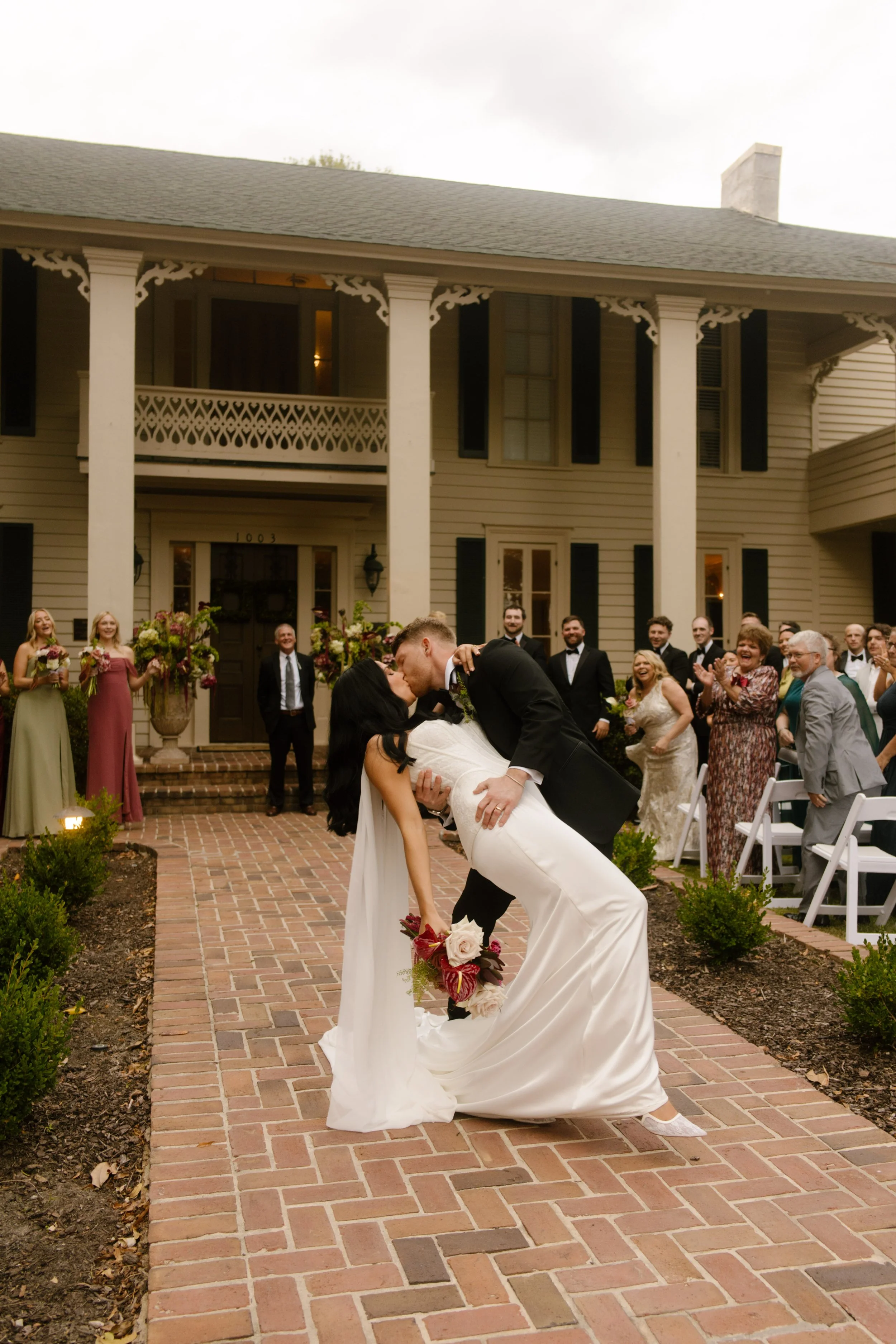 Bride and groom sharing a dramatic dip kiss on a brick walkway outside their historic wedding venue.