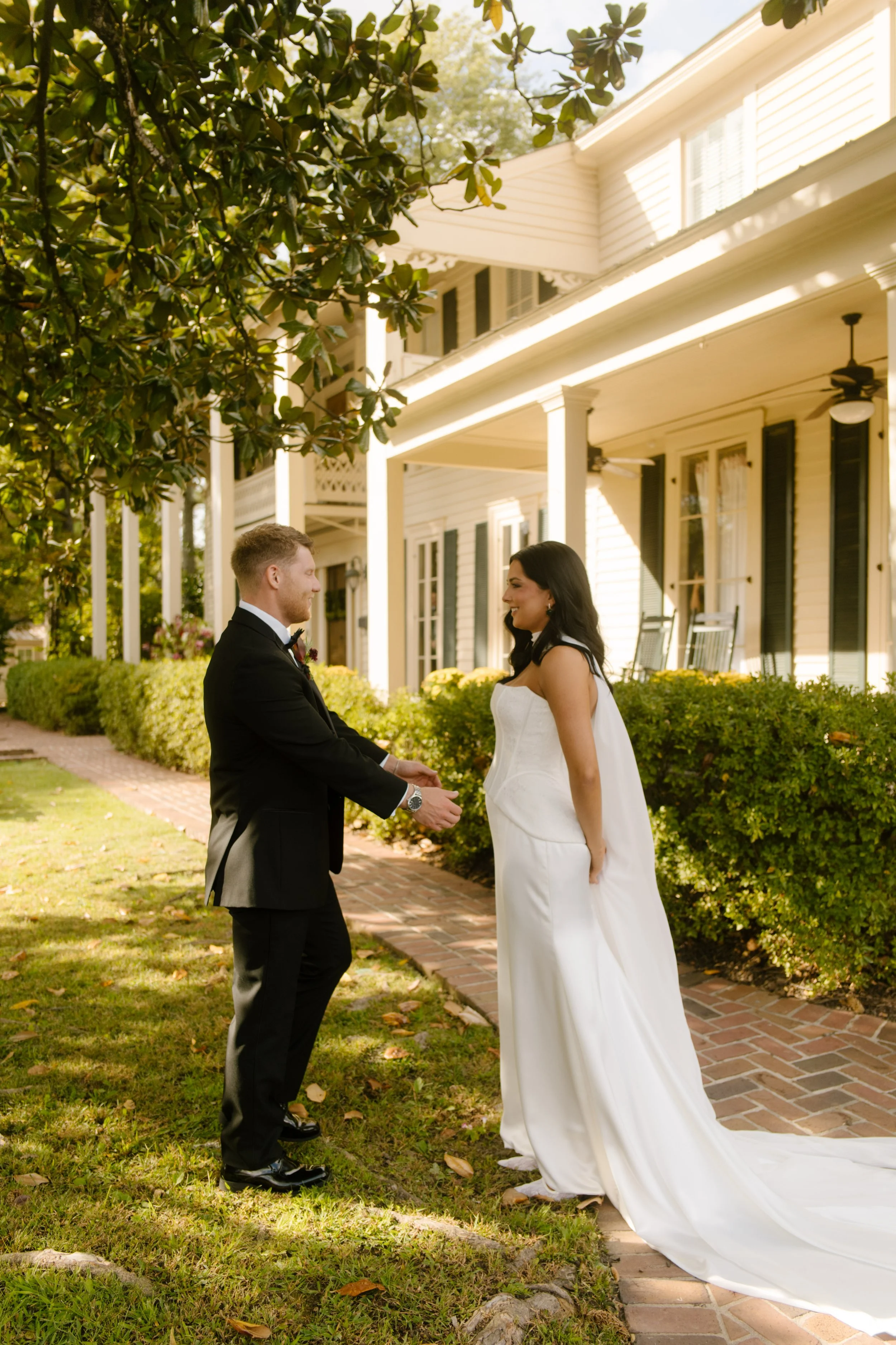 Bride and groom smiling at each other during their outdoor first look beside a historic white house.