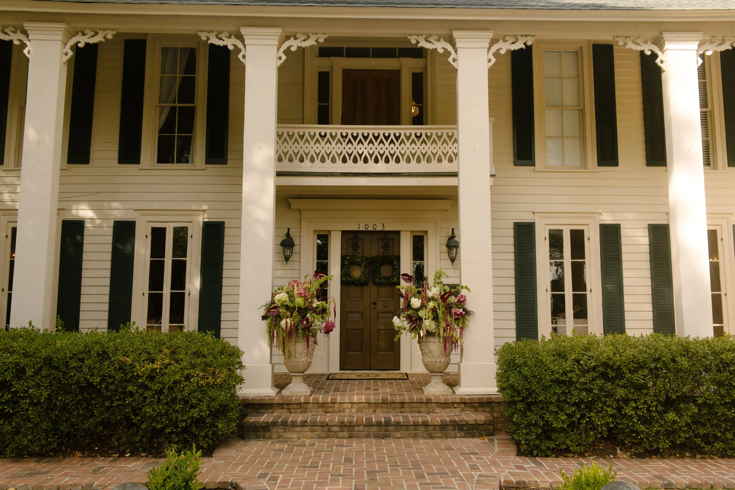 Historic white wedding venue with tall columns and floral arrangements featuring moody wedding colors of burgundy, pink, and green.