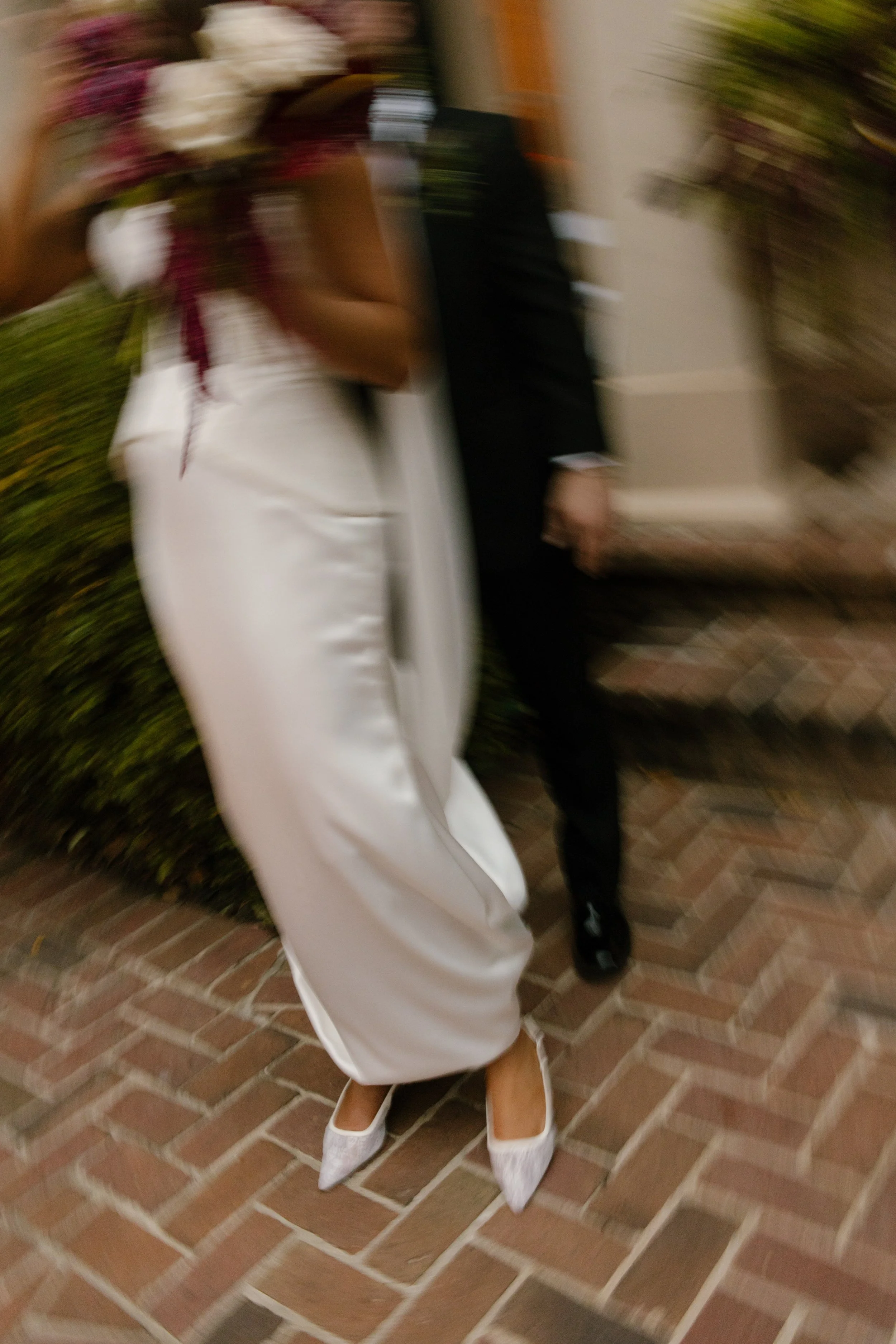 Motion-blur wedding portrait featuring moody wedding colors in burgundy and ivory florals as the bride walks outside with the groom.
