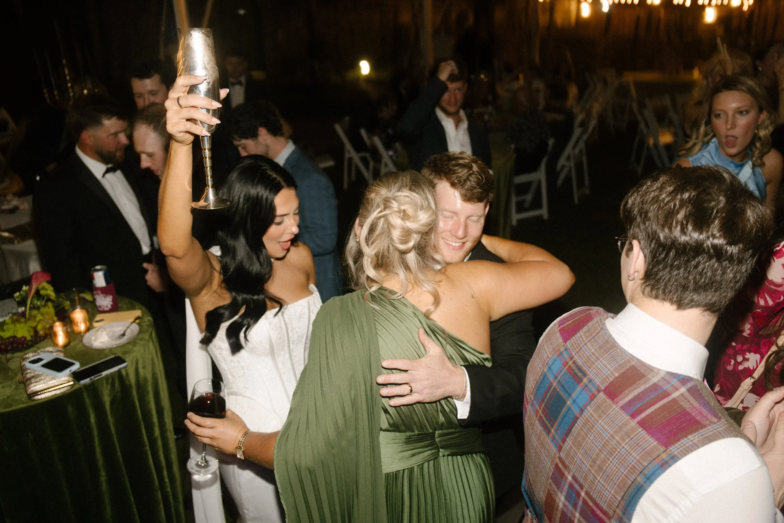 Bride celebrating on the dance floor with wedding guests wearing moody wedding colors of olive green and burgundy.