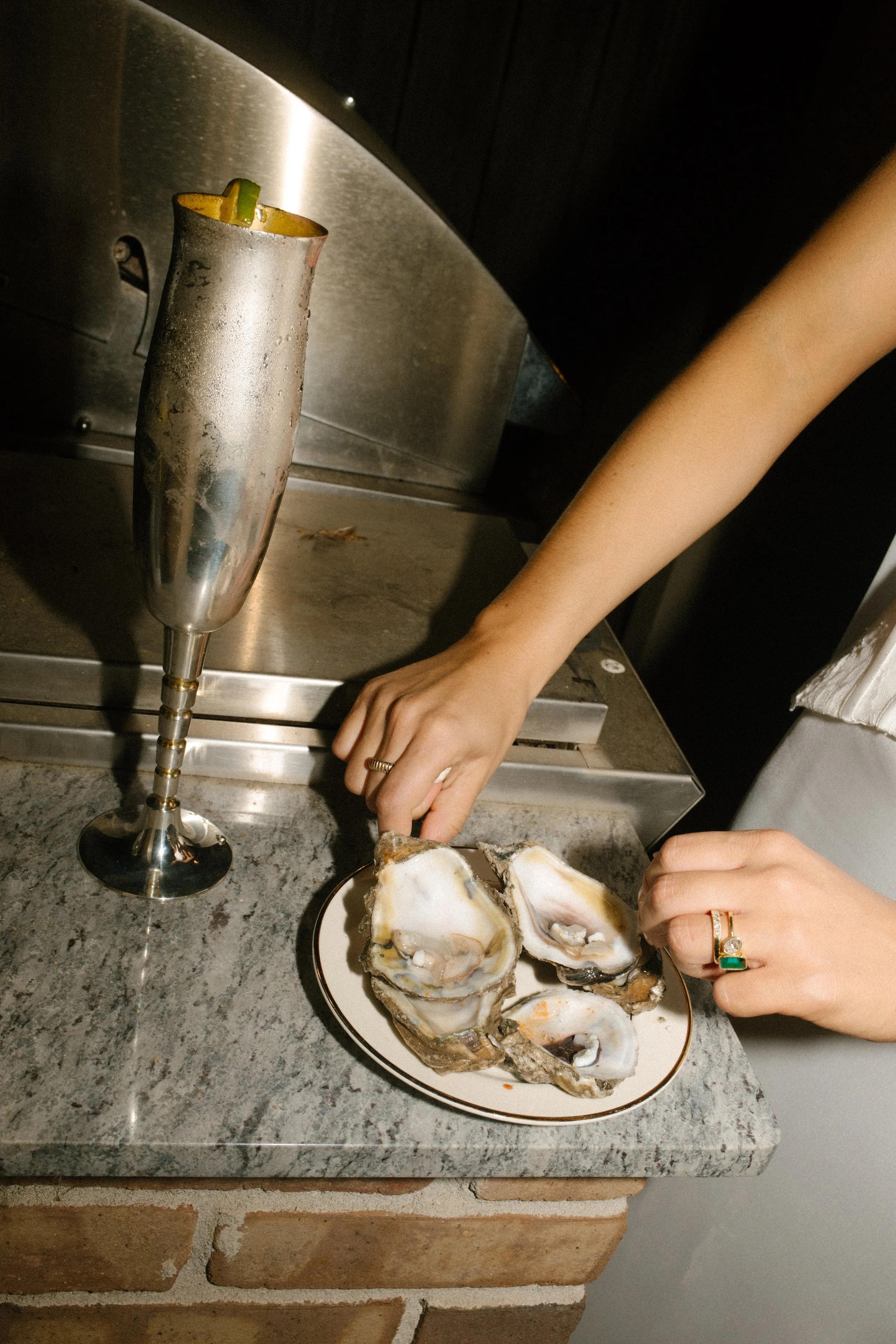 Bride enjoying oysters at her wedding reception beside a silver champagne flute and vintage-inspired details.