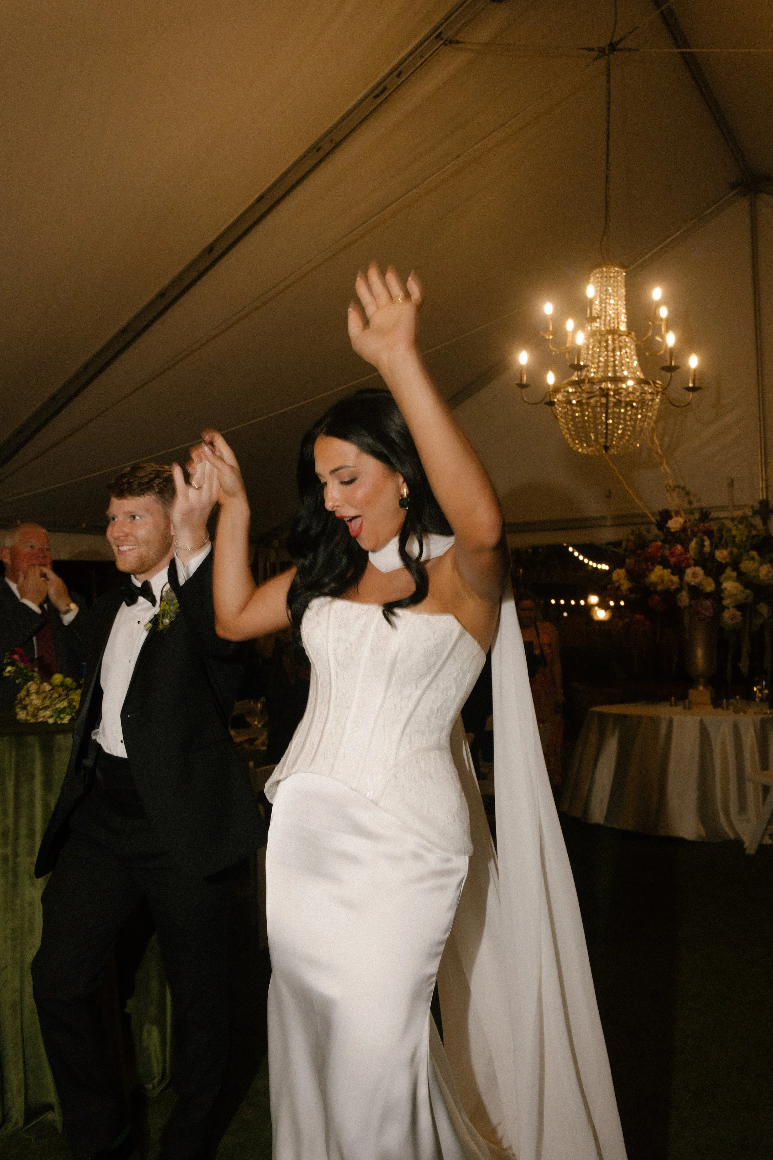 Bride and groom dancing beneath a chandelier at their wedding reception, surrounded by moody wedding colors and warm candlelit details.
