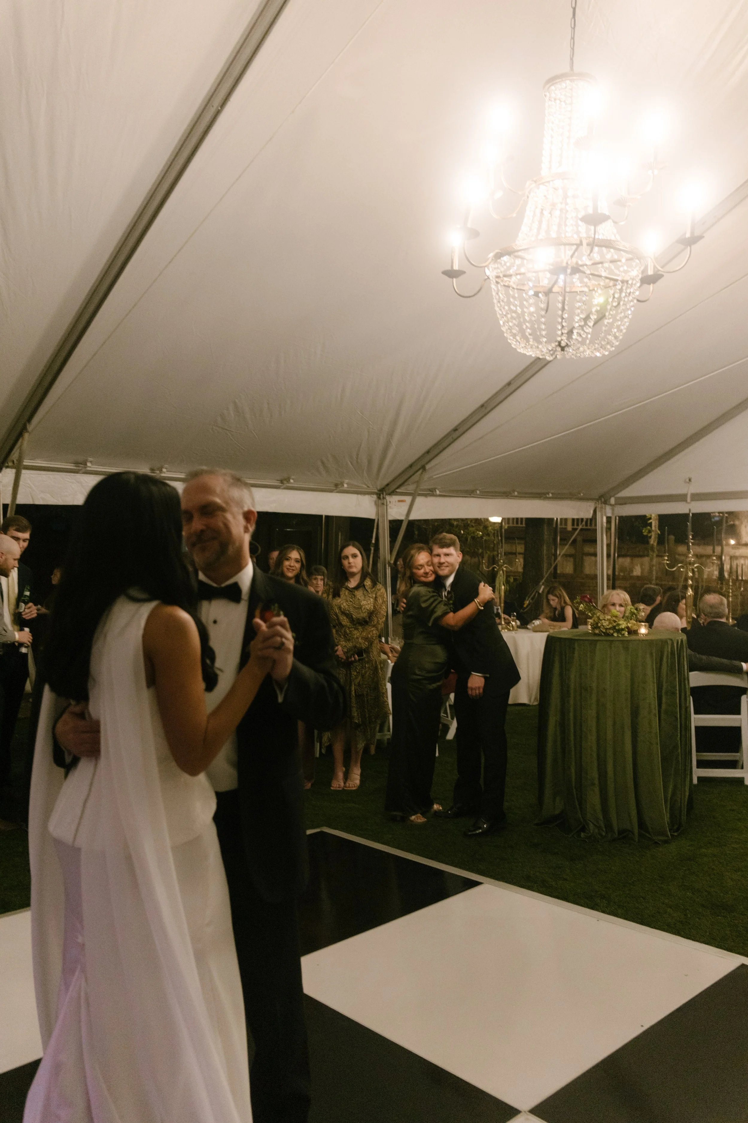 Bride sharing a dance with a family member during an intimate wedding reception beneath a chandelier.