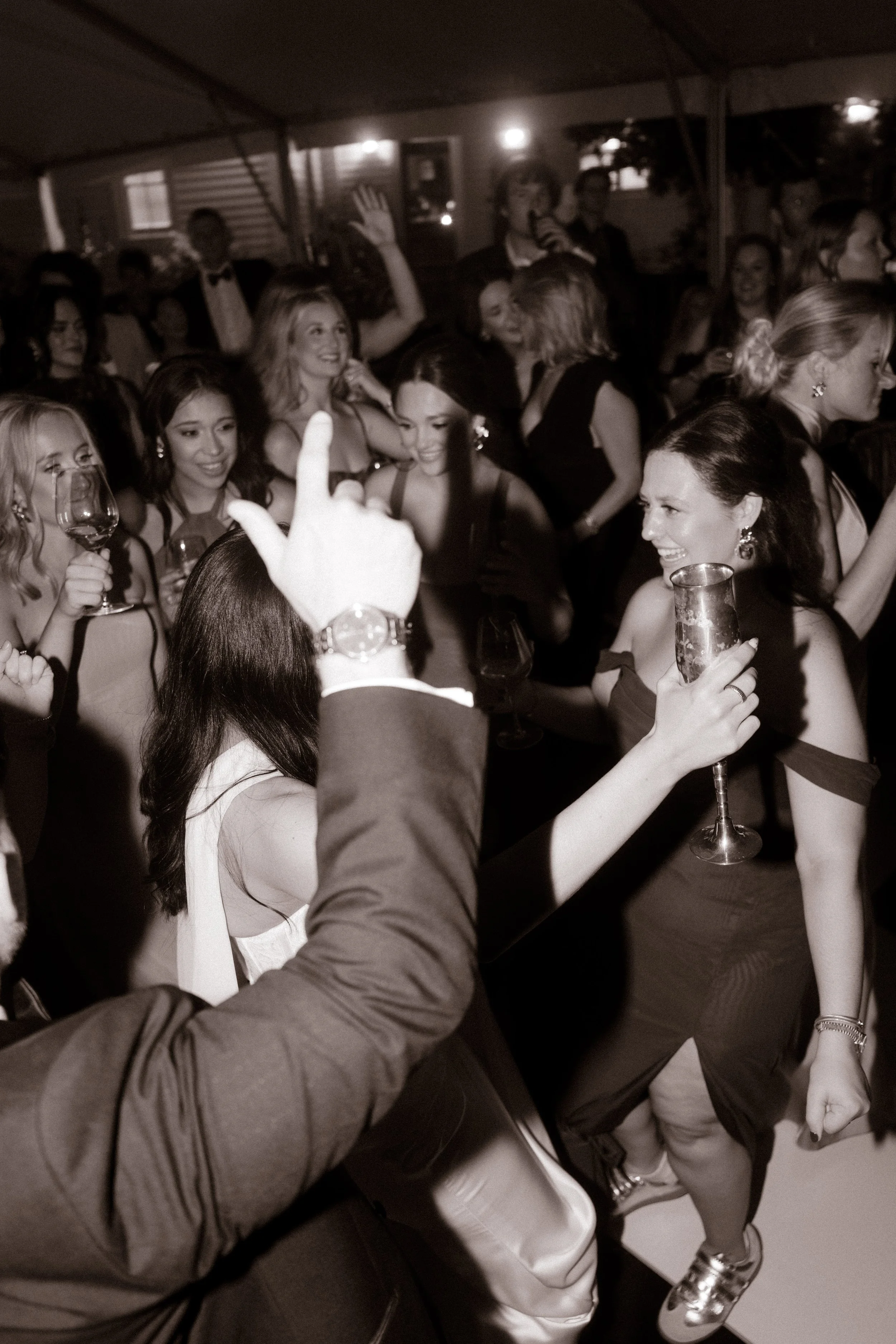 Black-and-white candid wedding reception photograph of guests dancing and celebrating in moody wedding colors.