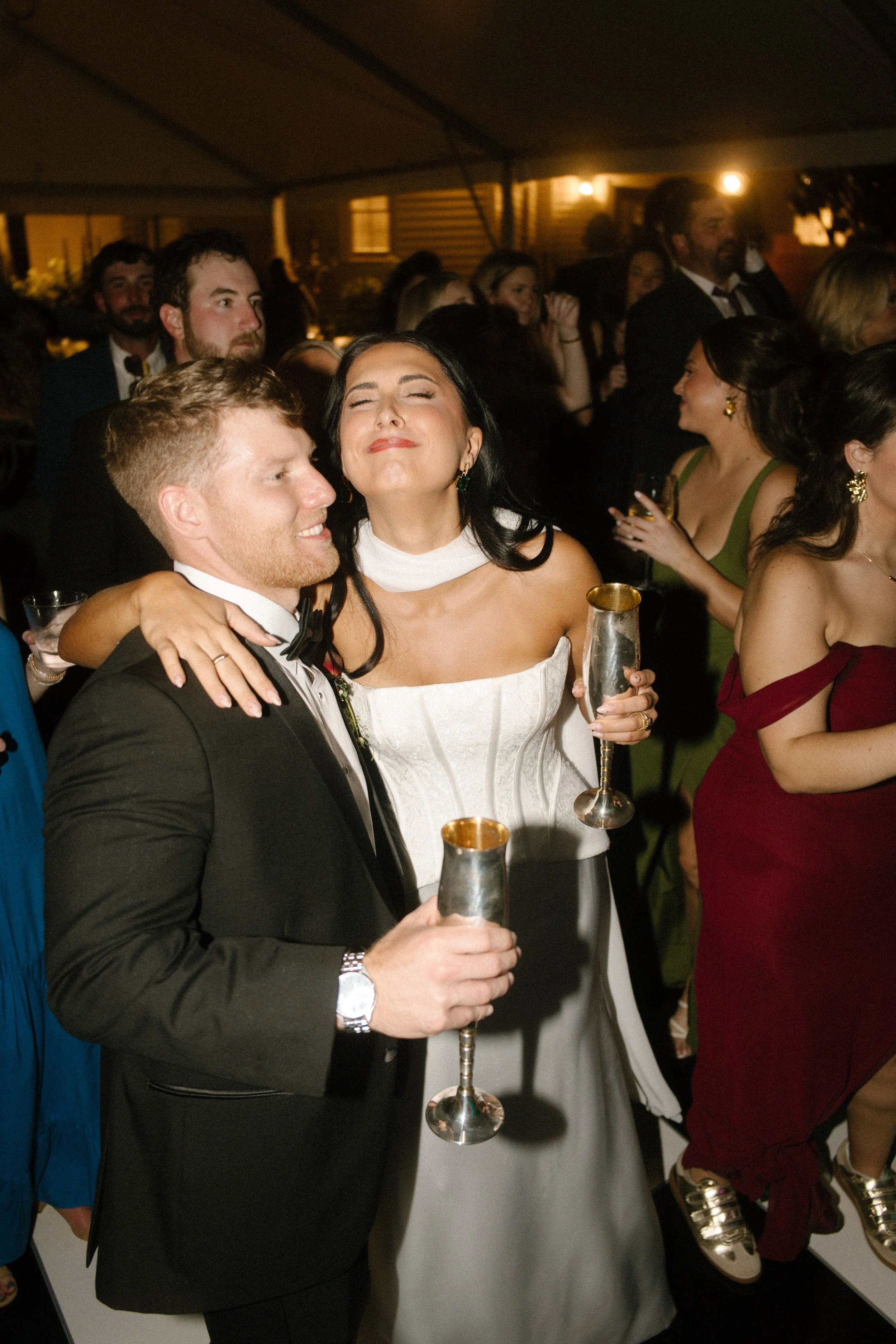 Bride and groom celebrating with silver champagne flutes during their lively nighttime wedding reception.