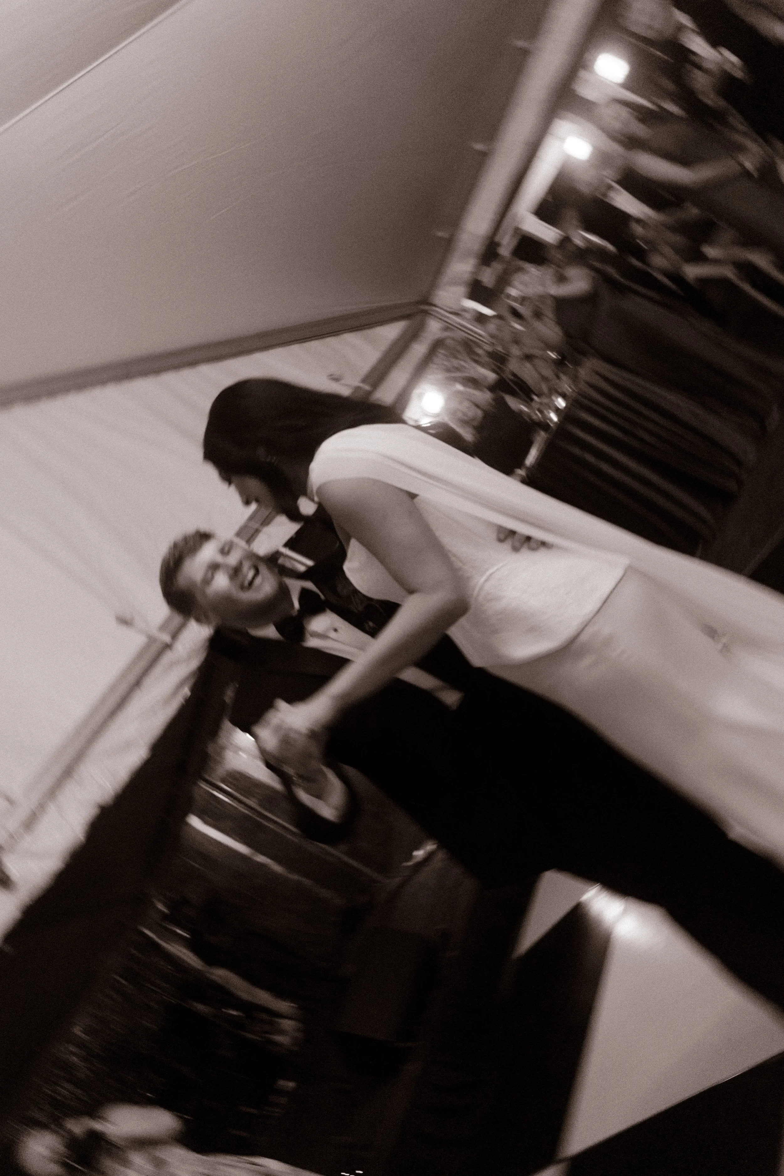 Black-and-white candid photograph of a bride and groom laughing together on the dance floor beneath a wedding reception tent.