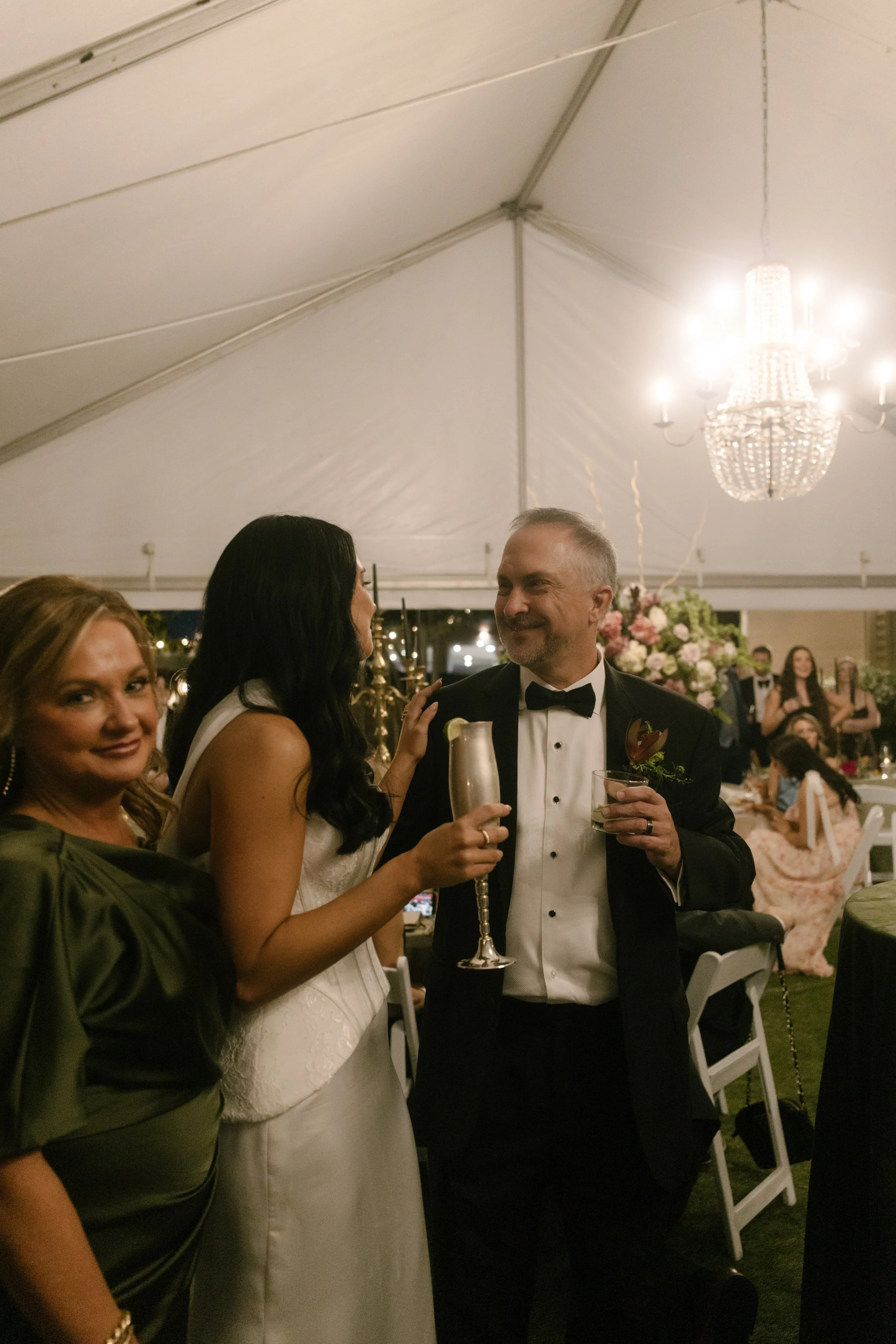 Bride celebrating with family beneath a chandelier at a wedding reception featuring moody wedding colors and olive green attire.