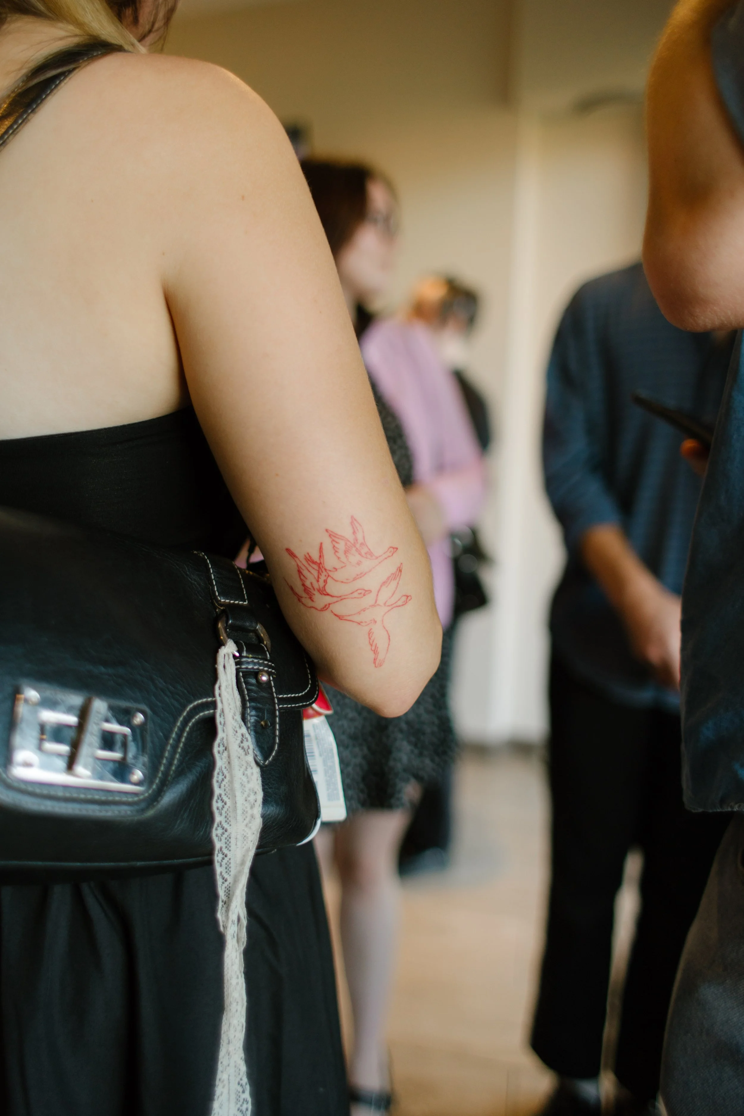 Close-up of a guest's red floral arm tattoo and black outfit during a casual baseball stadium rehearsal dinner.