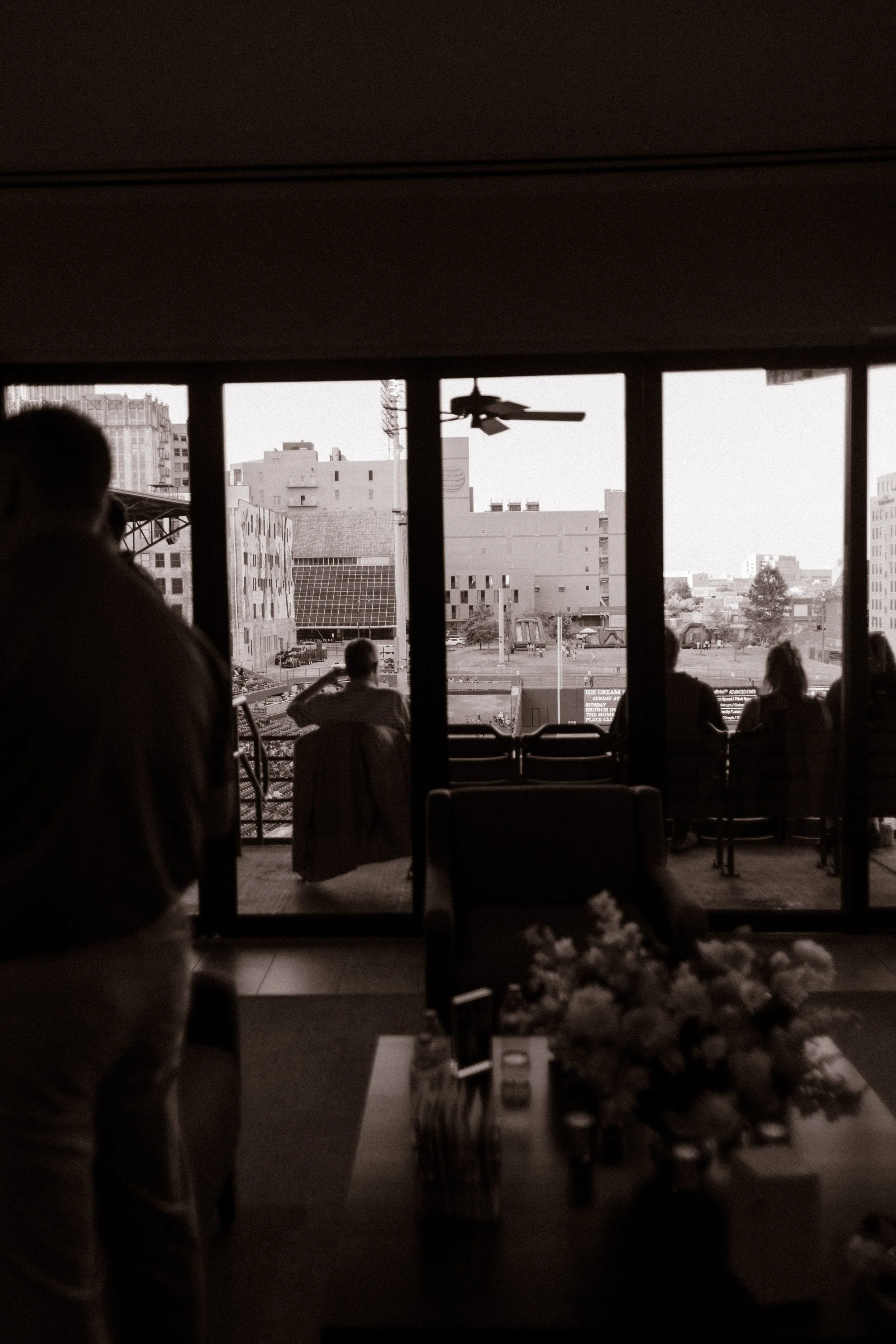 Black-and-white photograph of guests gathered on a stadium balcony overlooking the city, offering inspiration for fun engagement photos in unexpected locations.