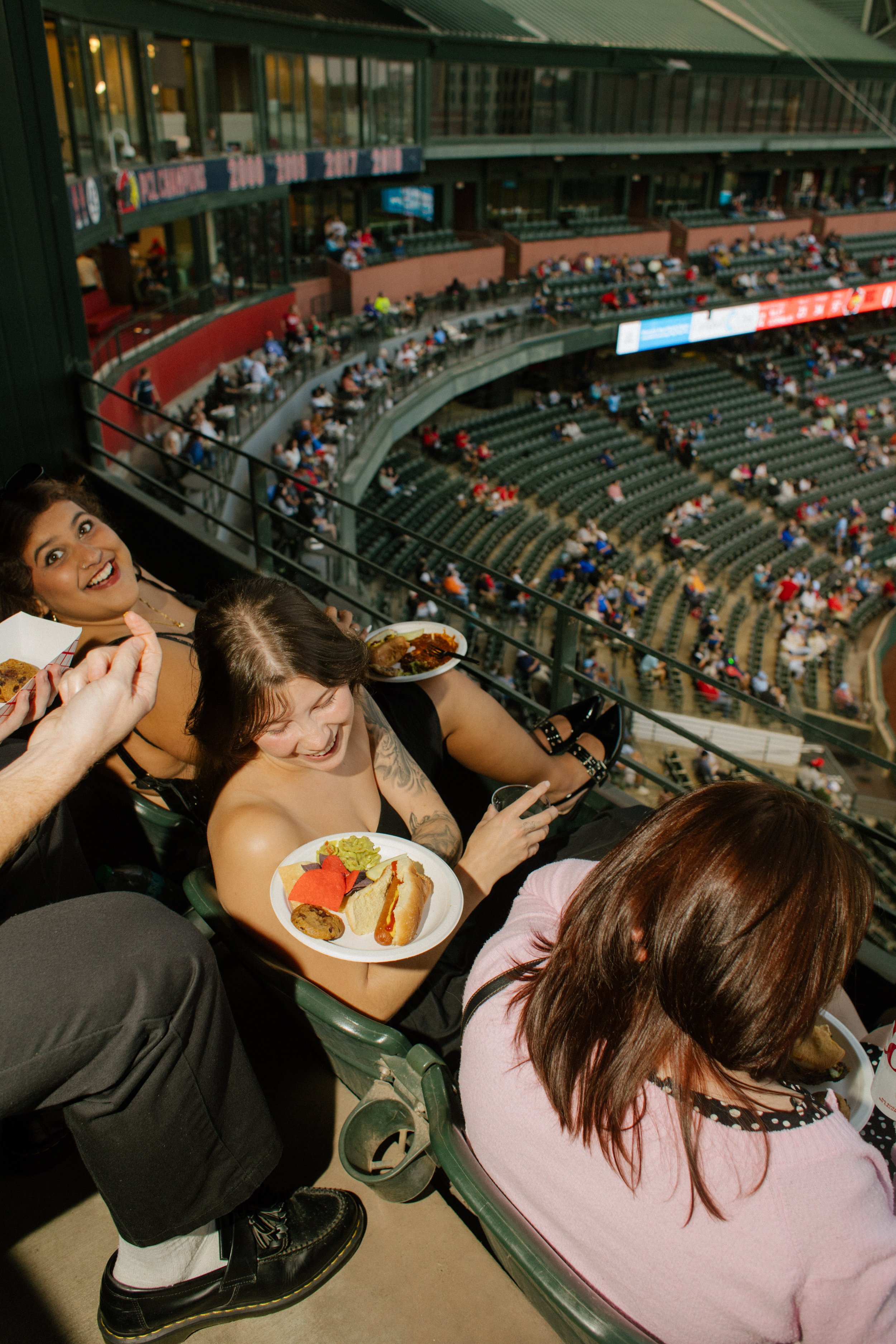 Candid overhead photograph of guests laughing, eating stadium food, and chatting in their seats, capturing the energy that makes fun engagement photos feel natural.