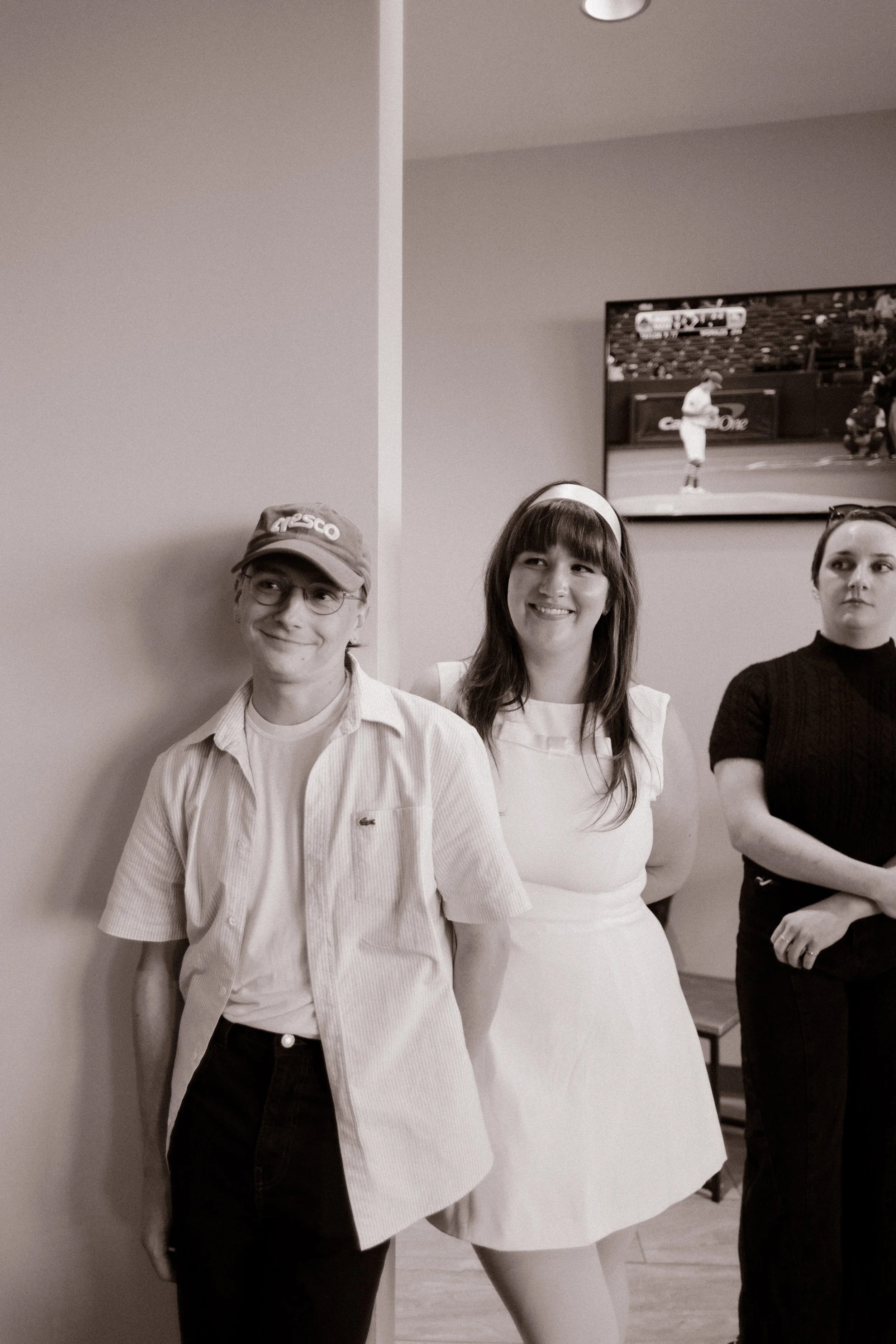 Black-and-white portrait of a couple in casual outfits standing together against a wall during their wedding rehearsal celebration.
