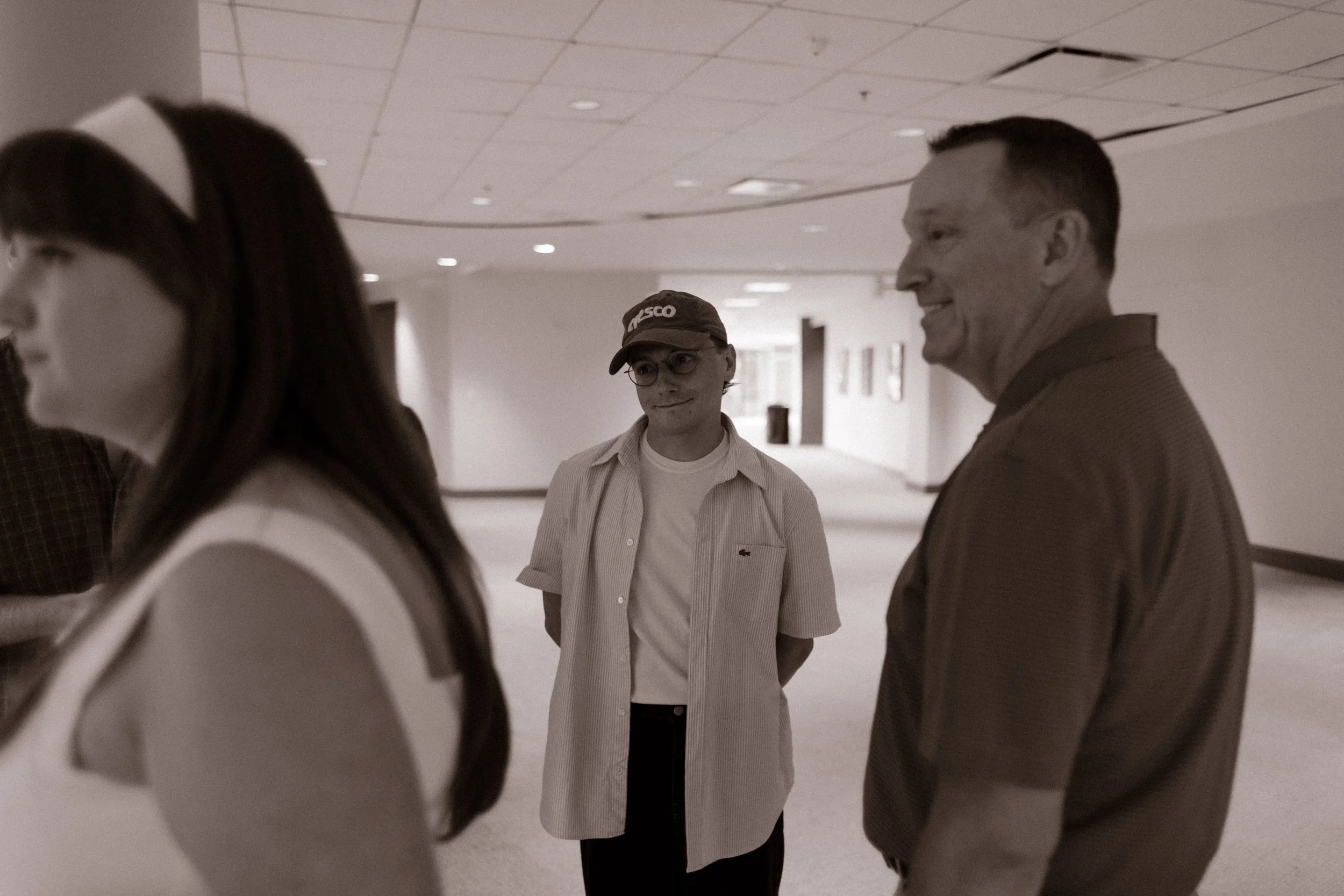 Black-and-white candid photograph of wedding rehearsal guests talking in a stadium hallway, reflecting the spontaneous interactions that inspire fun engagement photos.