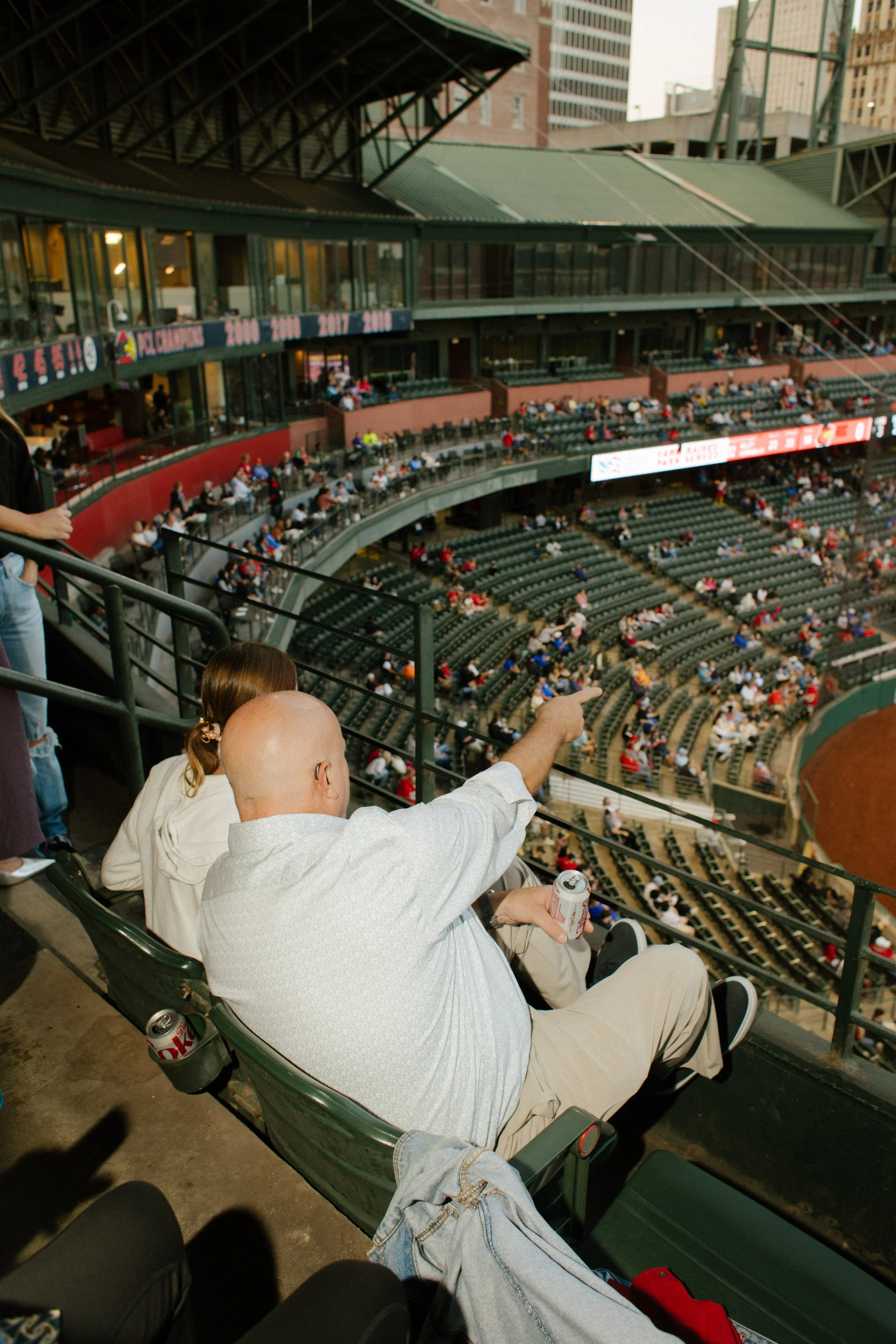 A guest points toward the baseball field from elevated stadium seats, capturing the relaxed atmosphere that inspires fun engagement photos at sporting events.