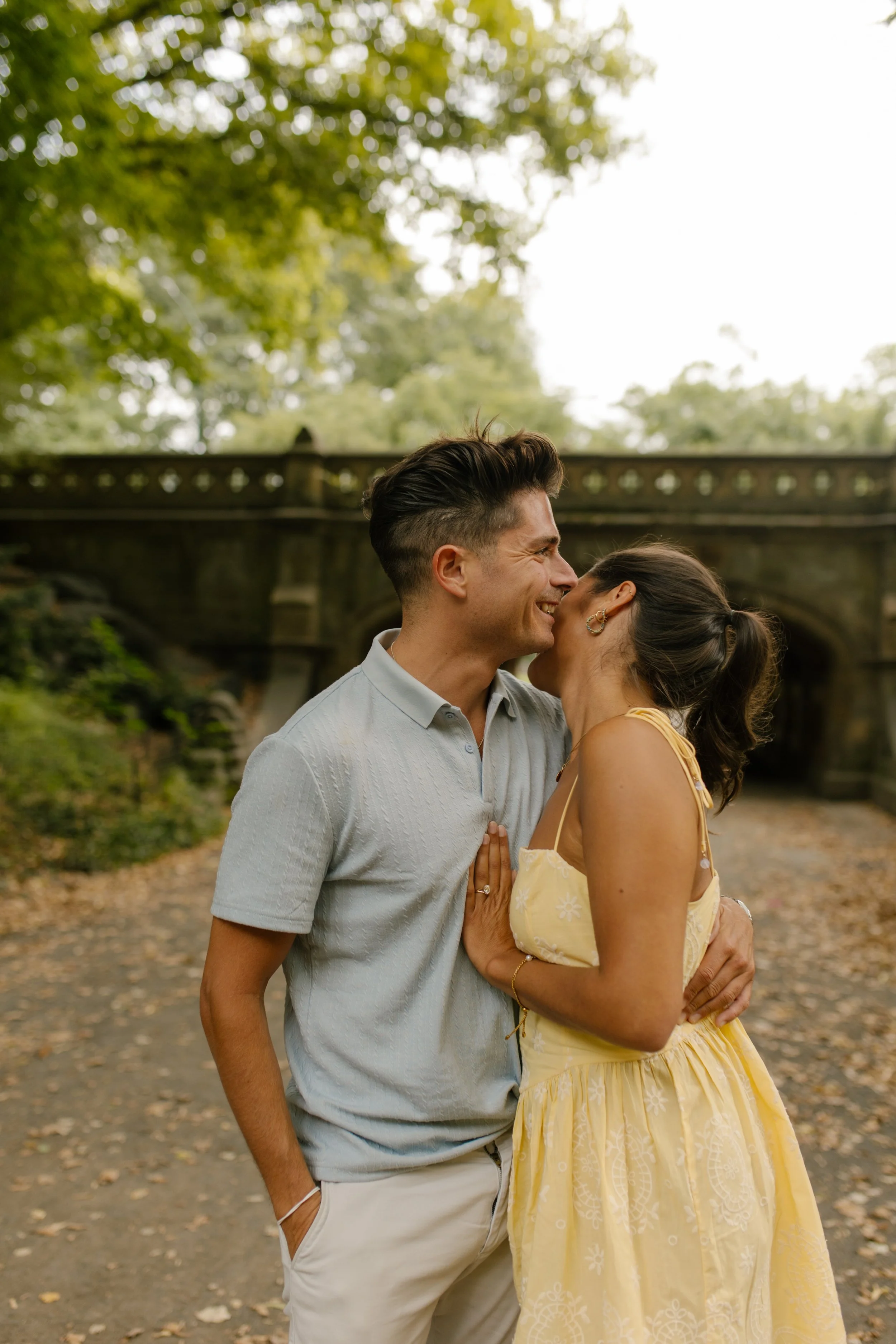 Chris kisses Sienna on the forehead as she smiles in her yellow dress following their surprise new york proposal in Central Park.