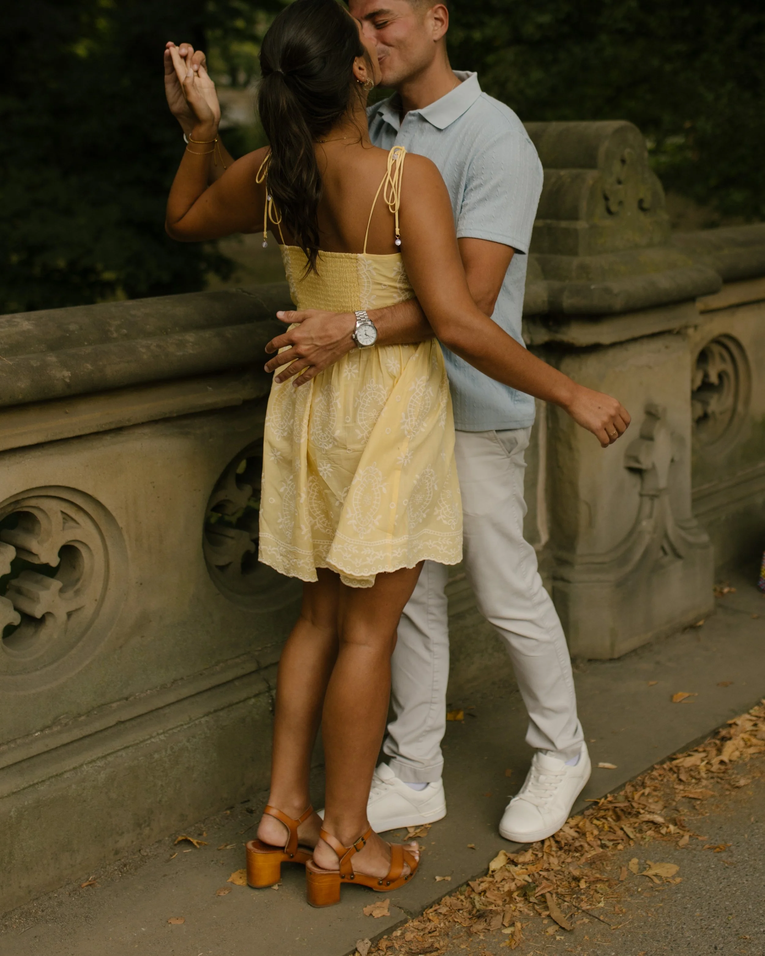Chris and Sienna share a kiss beside an ornate stone railing in Central Park, with Chris wrapping his arm around Sienna's waist.