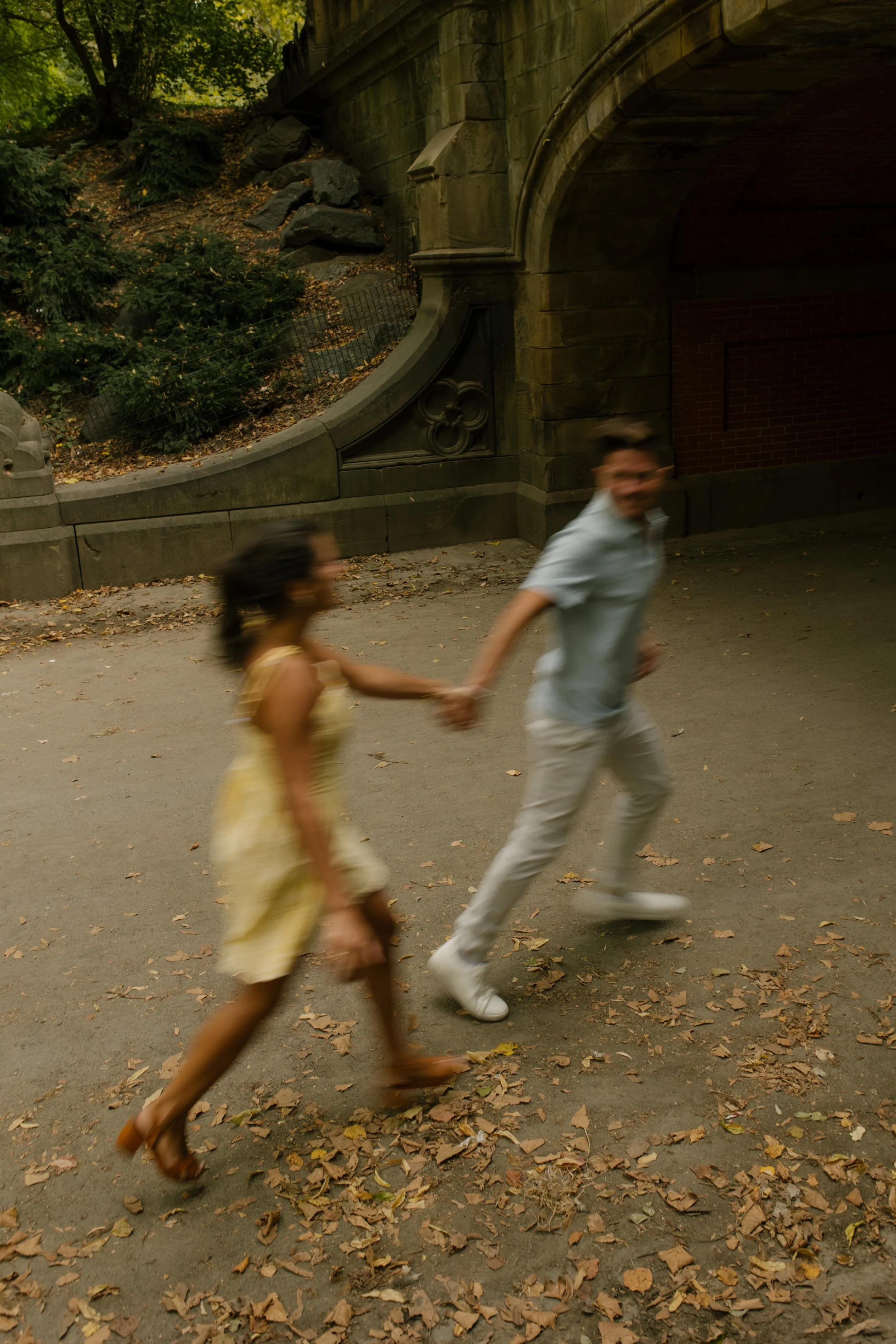 Chris leads Sienna by the hand as they run along a tree-lined Central Park pathway following their exciting new york proposal.