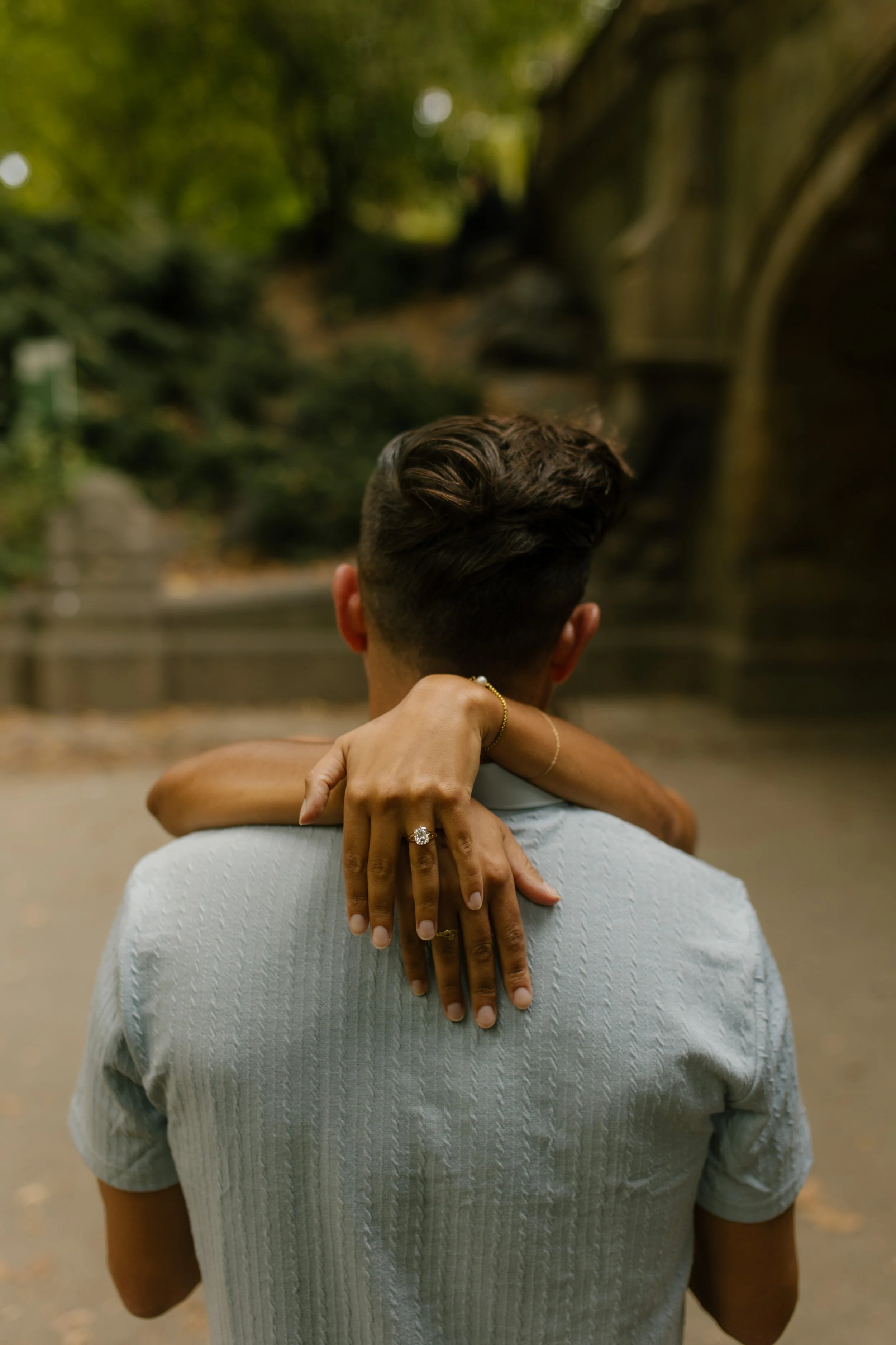 Close-up of Sienna's diamond engagement ring resting against Chris's shoulder as they embrace following their intimate new york proposal.