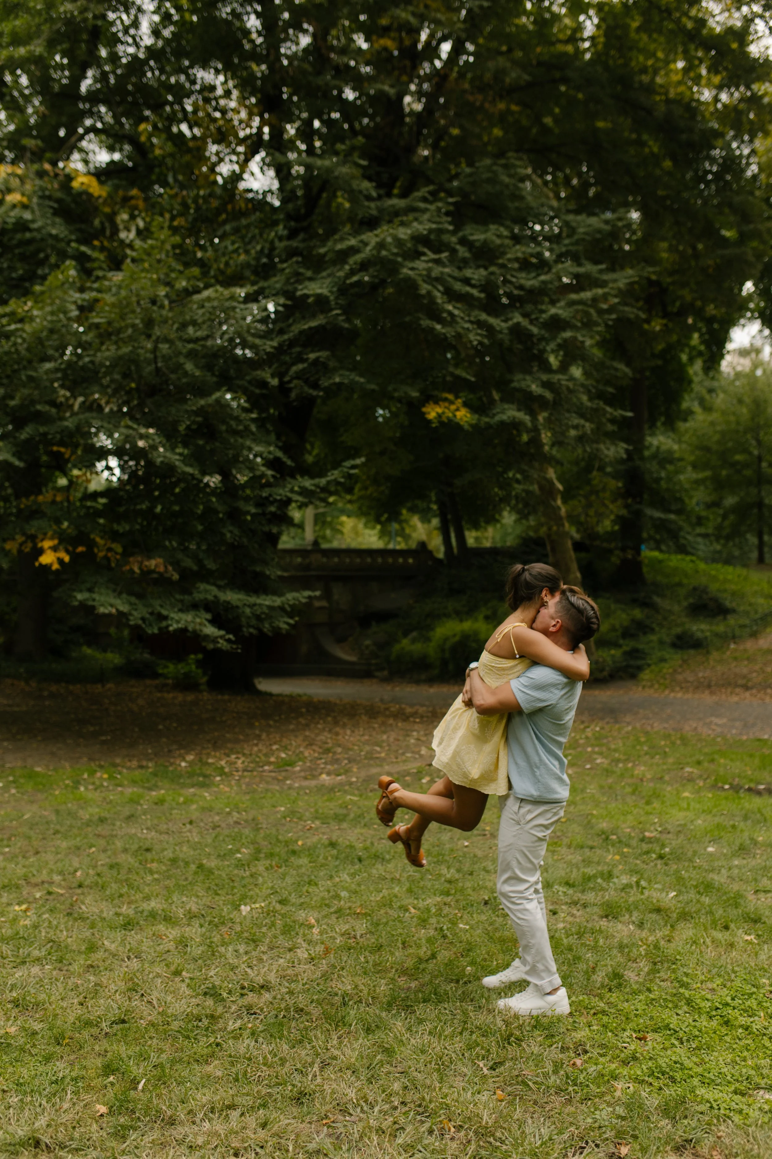 Chris lifts Sienna into his arms as she wraps one leg around him during their joyful new york proposal celebration on a grassy lawn in Central Park.