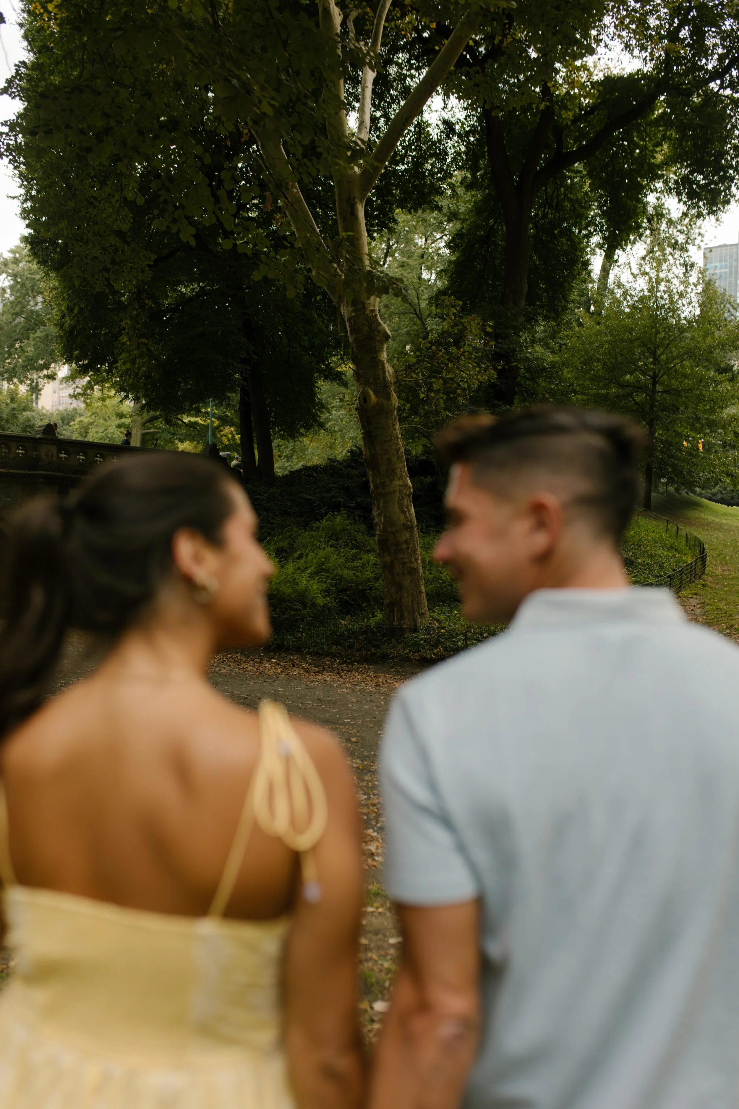 Candid photograph of Chris and Sienna walking hand in hand through Central Park, with leafy trees and a winding pathway ahead of them