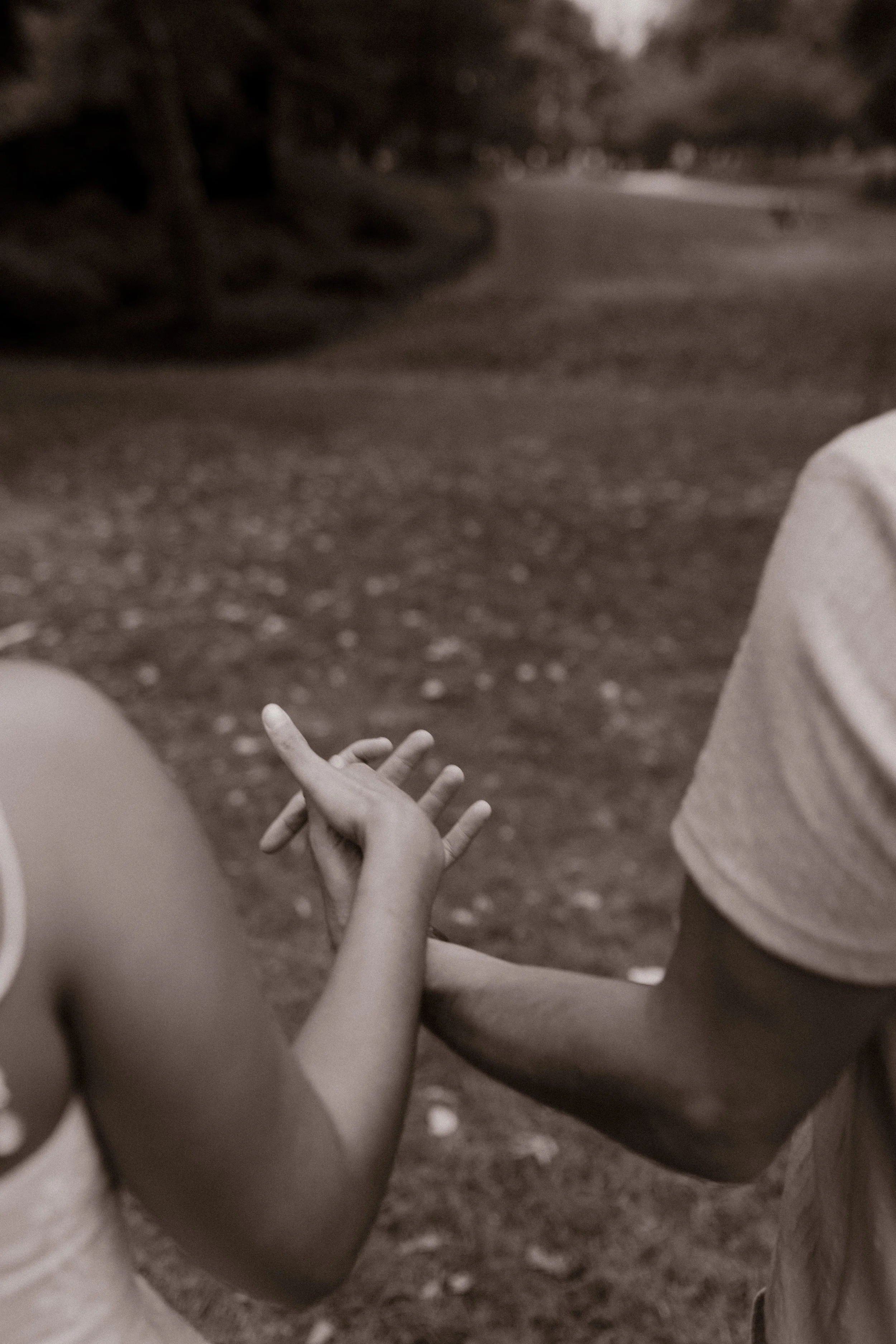 Black-and-white close-up of Chris and Sienna holding hands while walking together along a park pathway following their new york proposal.
