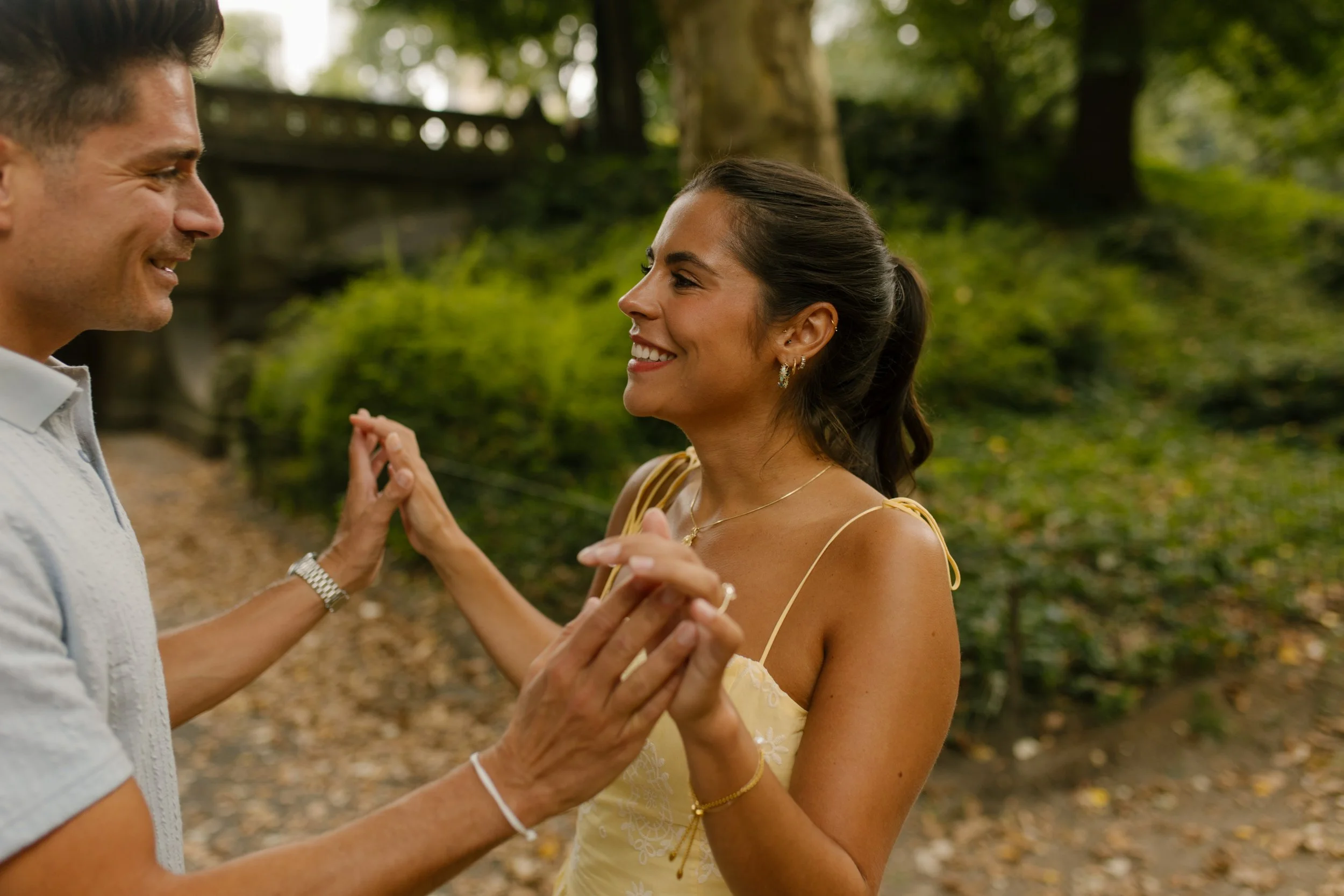 Chris and Sienna smile at each other while holding hands, capturing the excitement following their surprise new york proposal in Central Park.