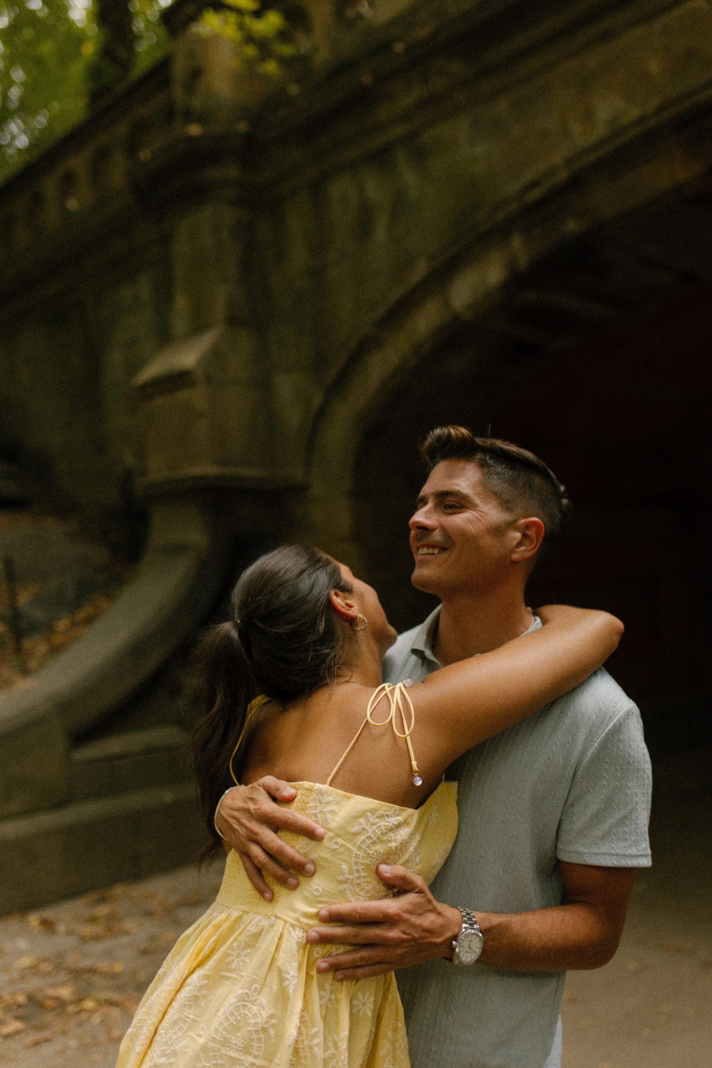 Chris wraps his arms around Sienna as she leans into him beneath a historic stone bridge in Central Park.