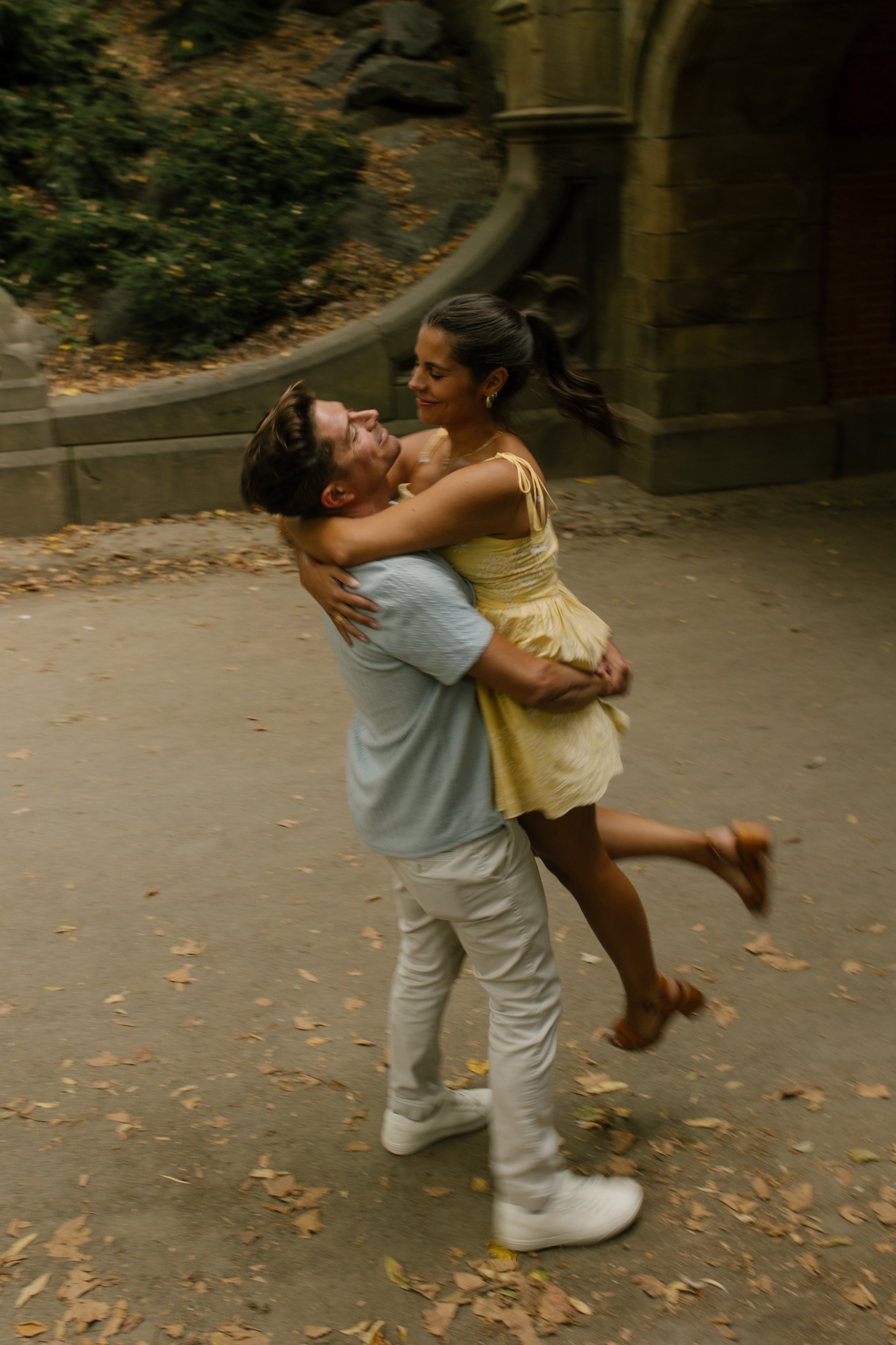 Chris lifts Sienna off the ground as she wraps her arms around his neck during their joyful new york proposal celebration beneath a Central Park stone archway.