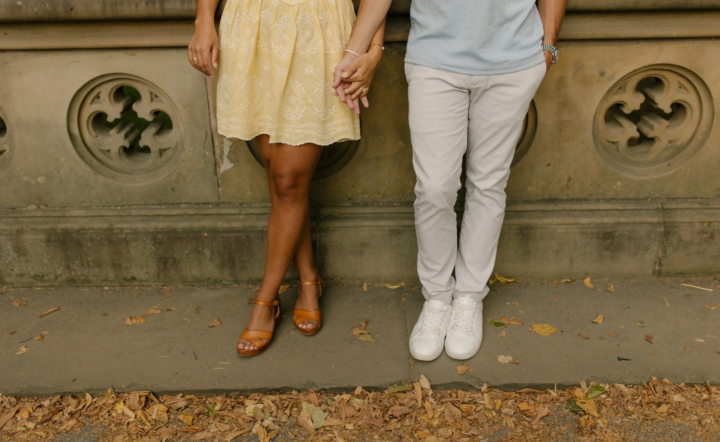 Sienna smiles down at her diamond engagement ring while standing in her pale yellow floral dress, admiring the newest addition following her new york proposal in Central Park.
