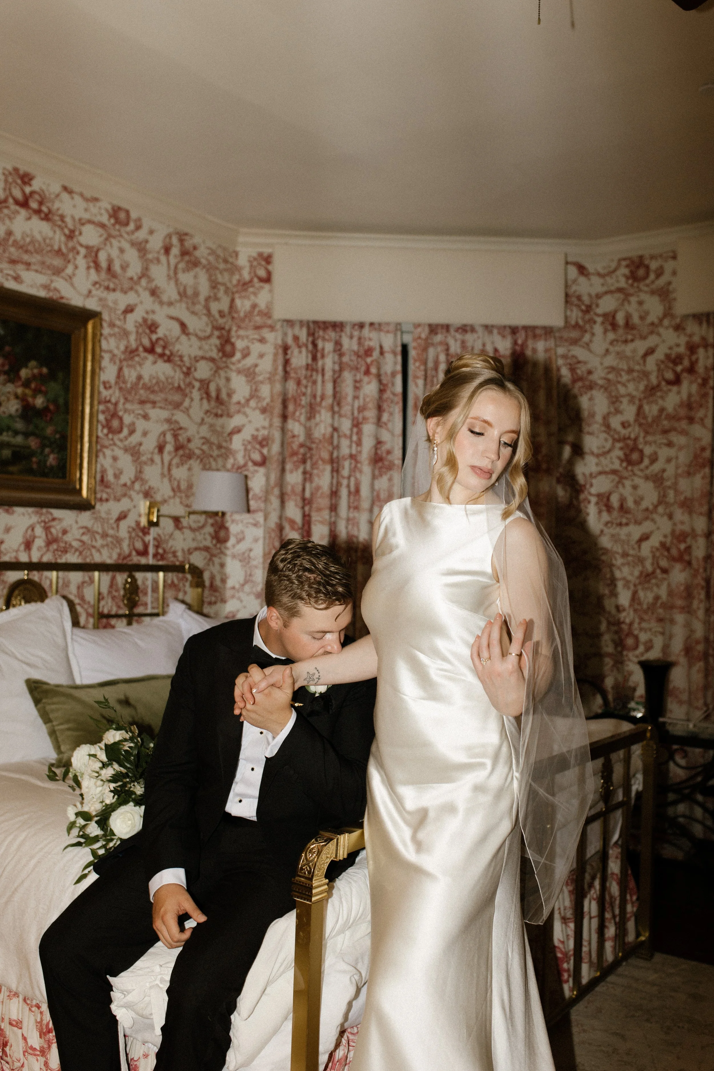 A romantic moment between a bride in a silk wedding gown and her groom in a vintage hotel room, artfully documented by a destination wedding photographer.
