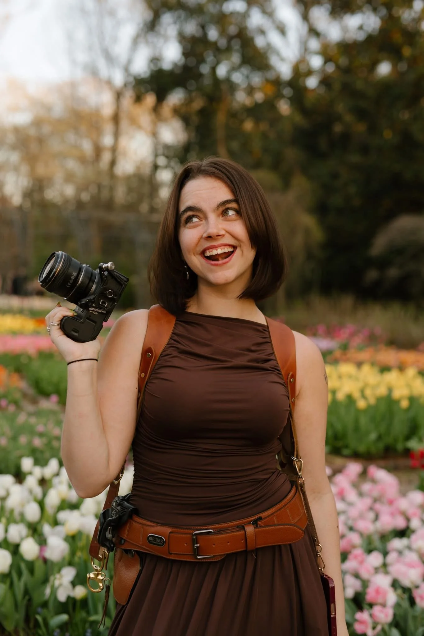 Wedding photographer smiling while holding her camera in a colorful garden during a fall wedding.