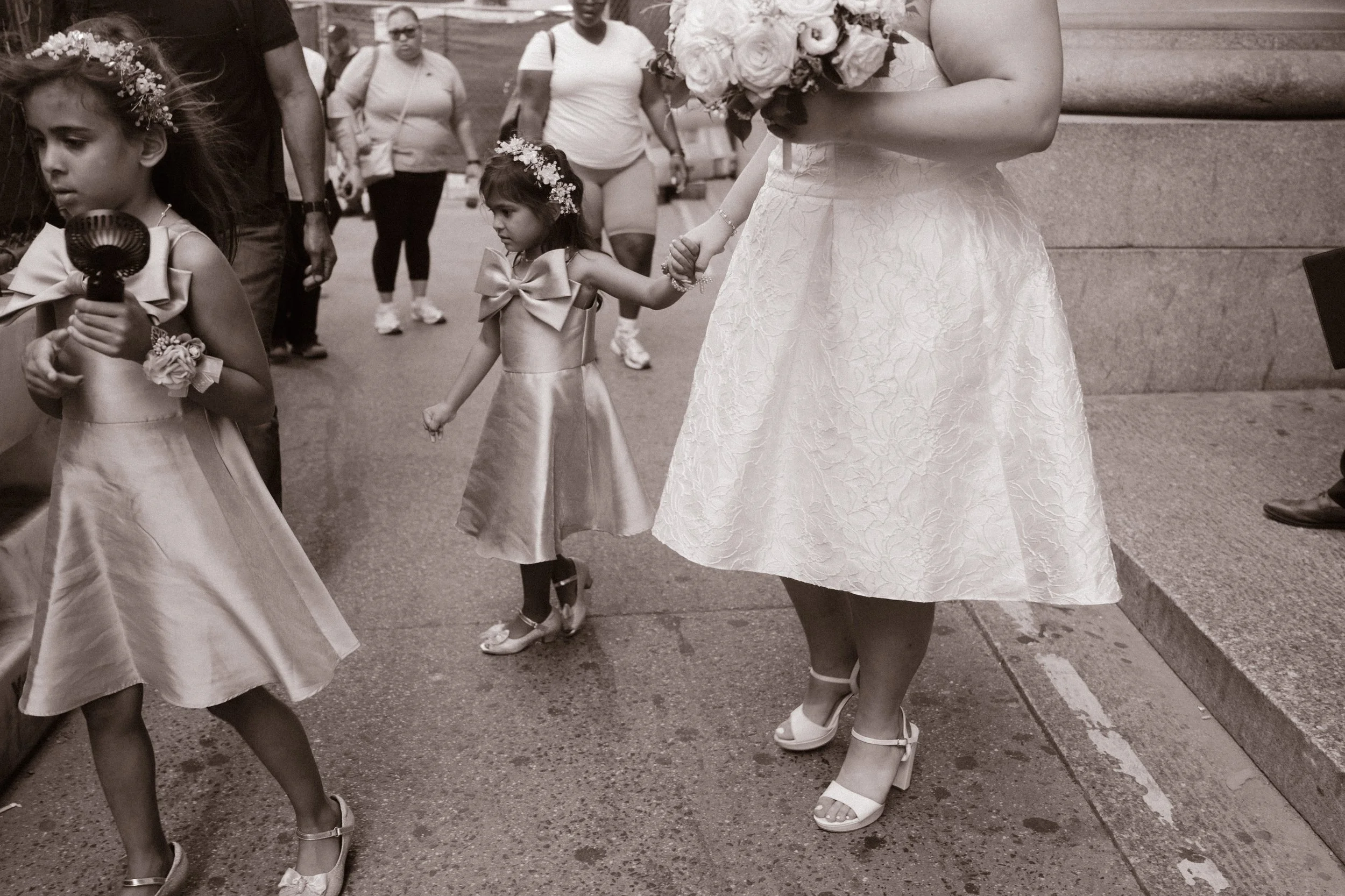 Black-and-white candid of flower girls walking with the bride during a New York City wedding.