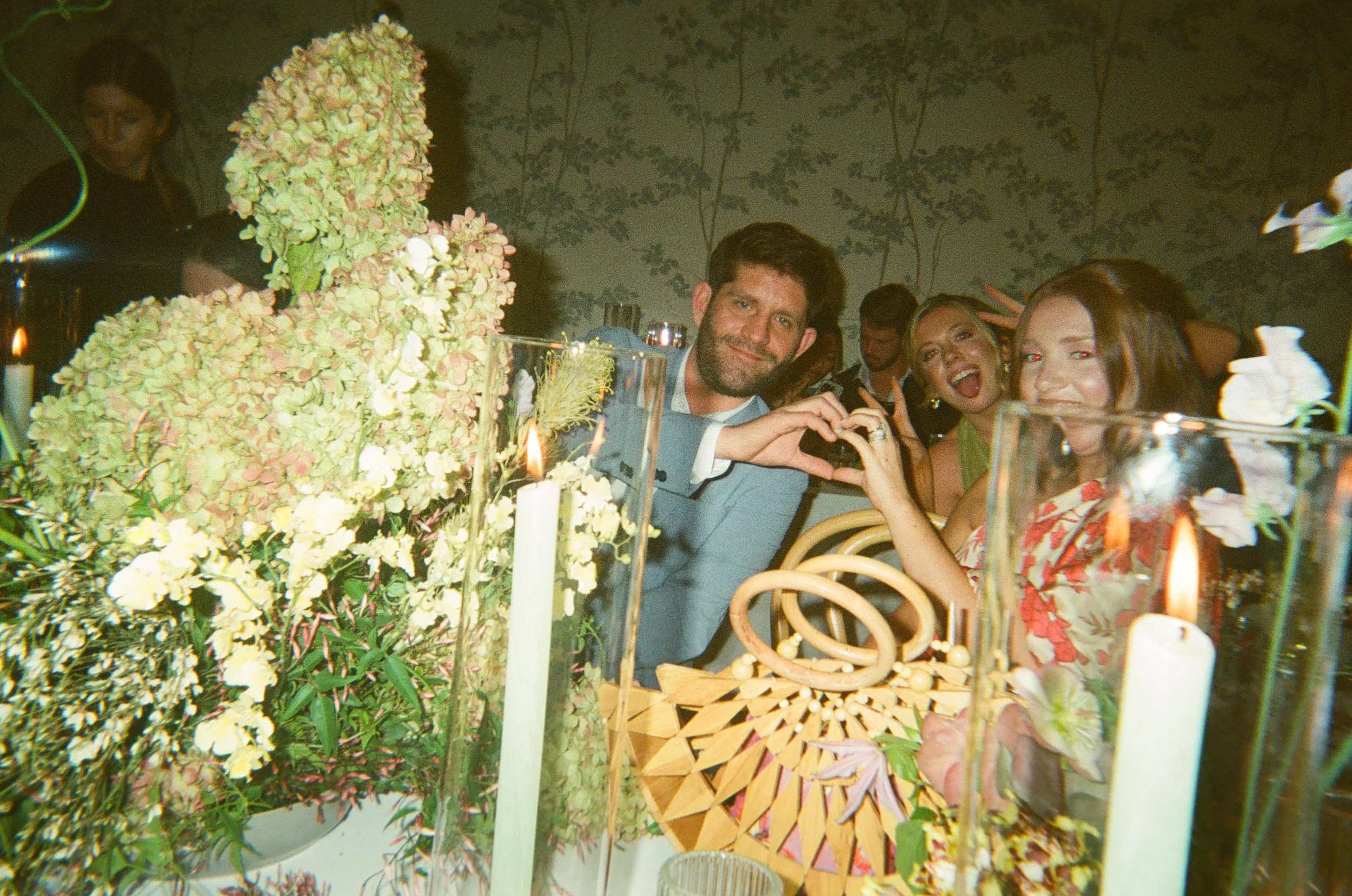 Guests making heart hands and posing playfully behind candlelit centerpieces.