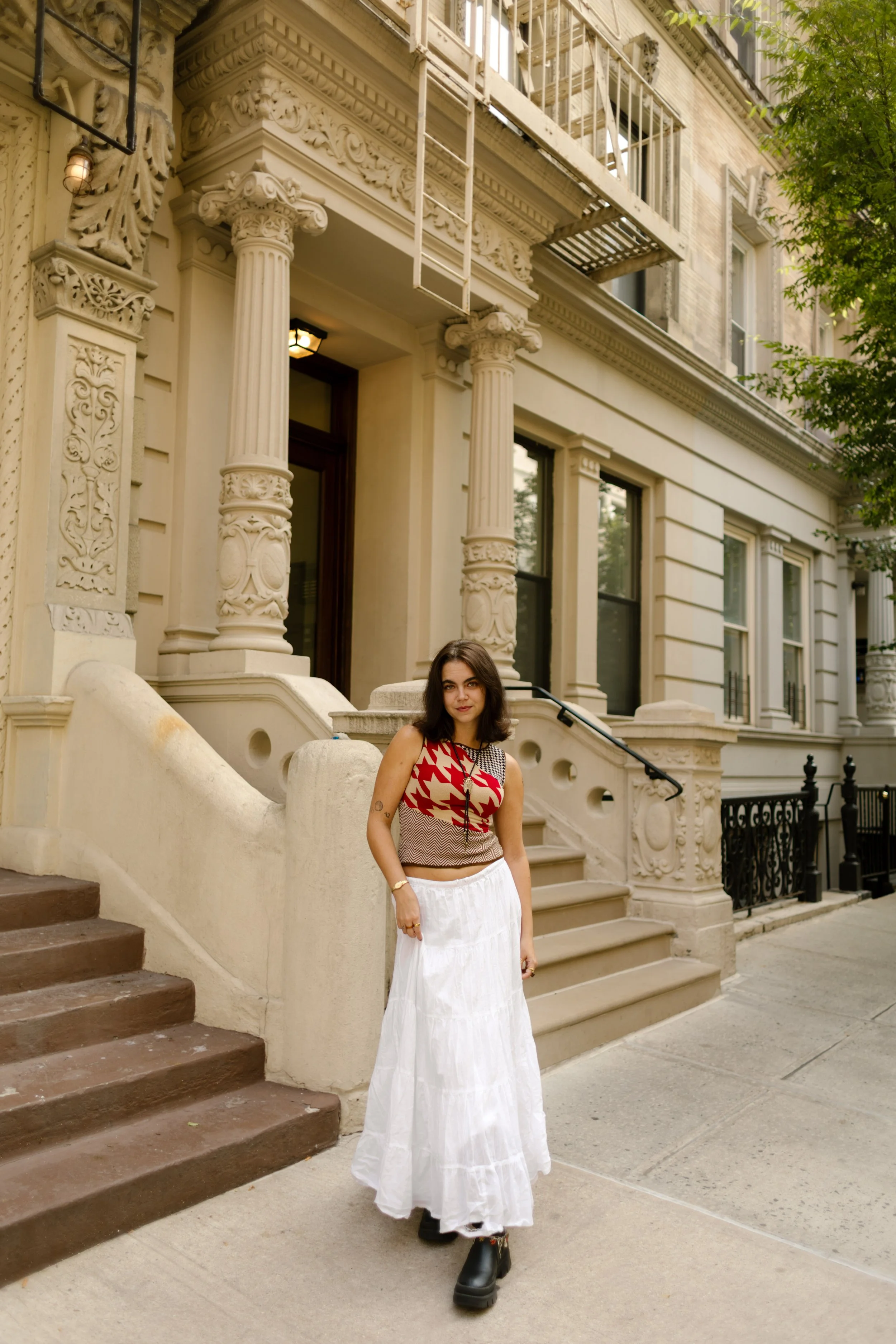 Woman posing outside a brownstone in a patterned top and long white skirt during a New York City portrait session.