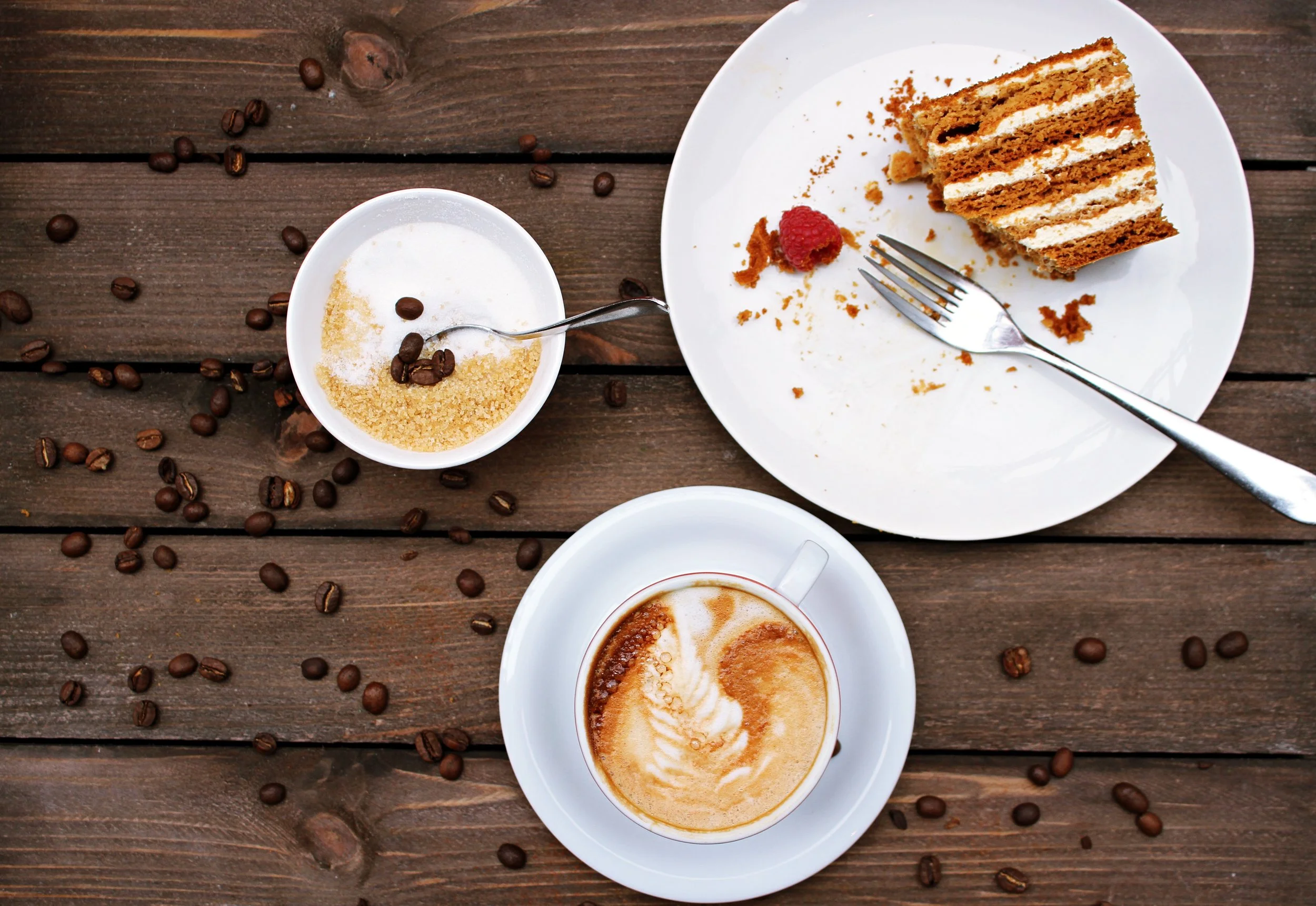 Image: half eaten cake and spoon positioned to side with sugar bowl and latte on table