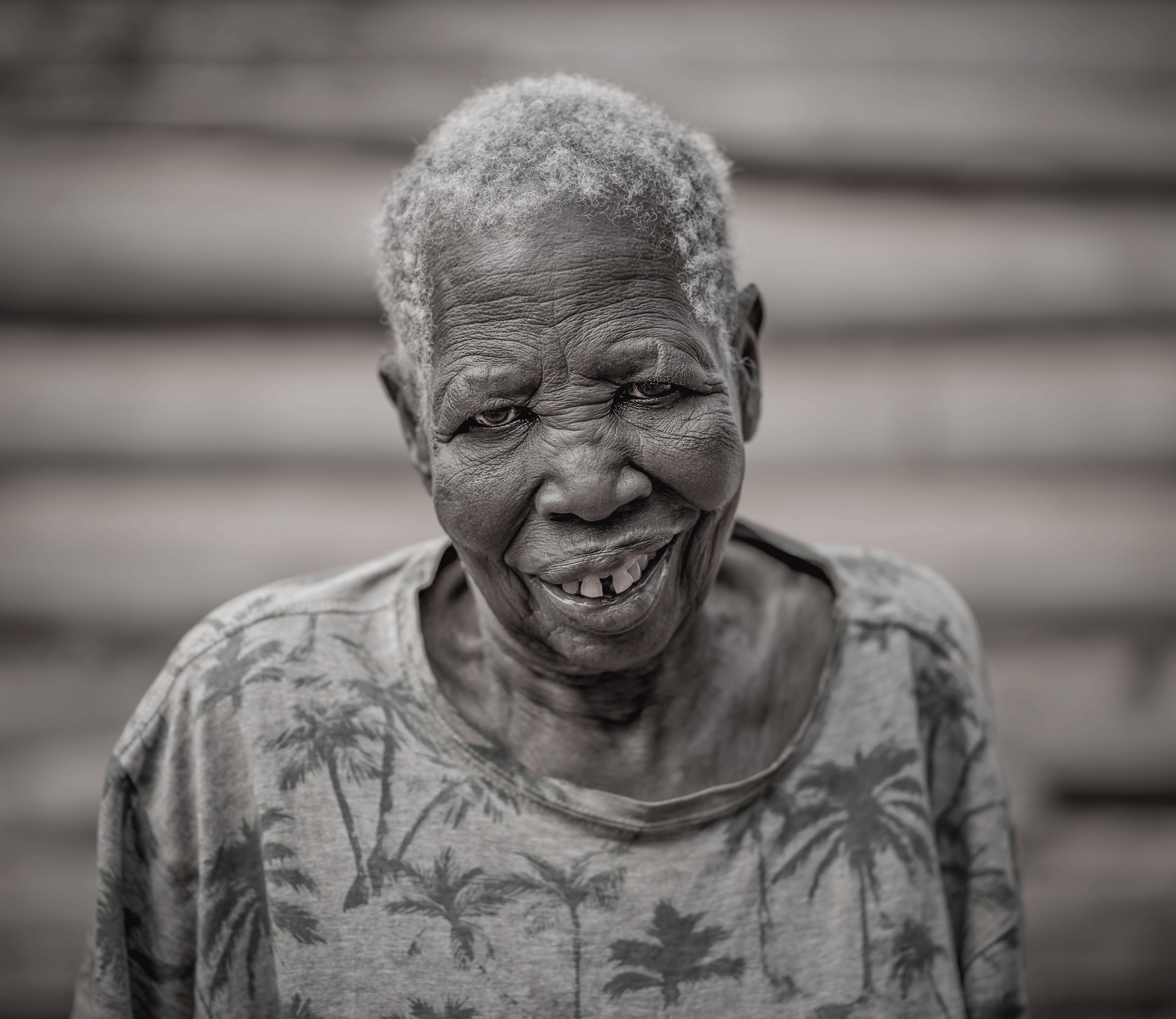 A smiling elderly African American woman with short gray hair, wearing a patterned top.