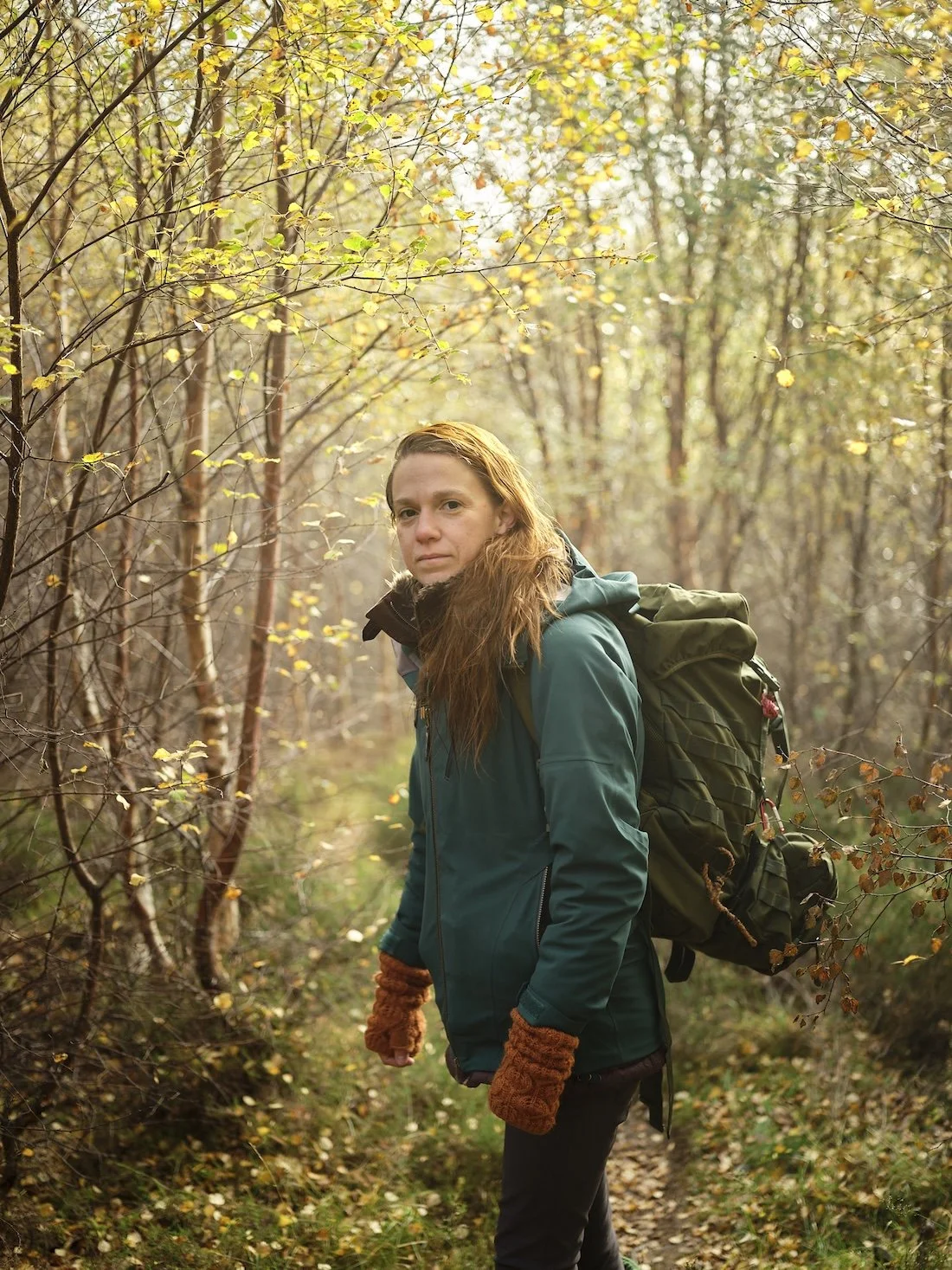 Local mountain and wild swimming guide Annie Armstrong standing with her backpack among an avenue of trees