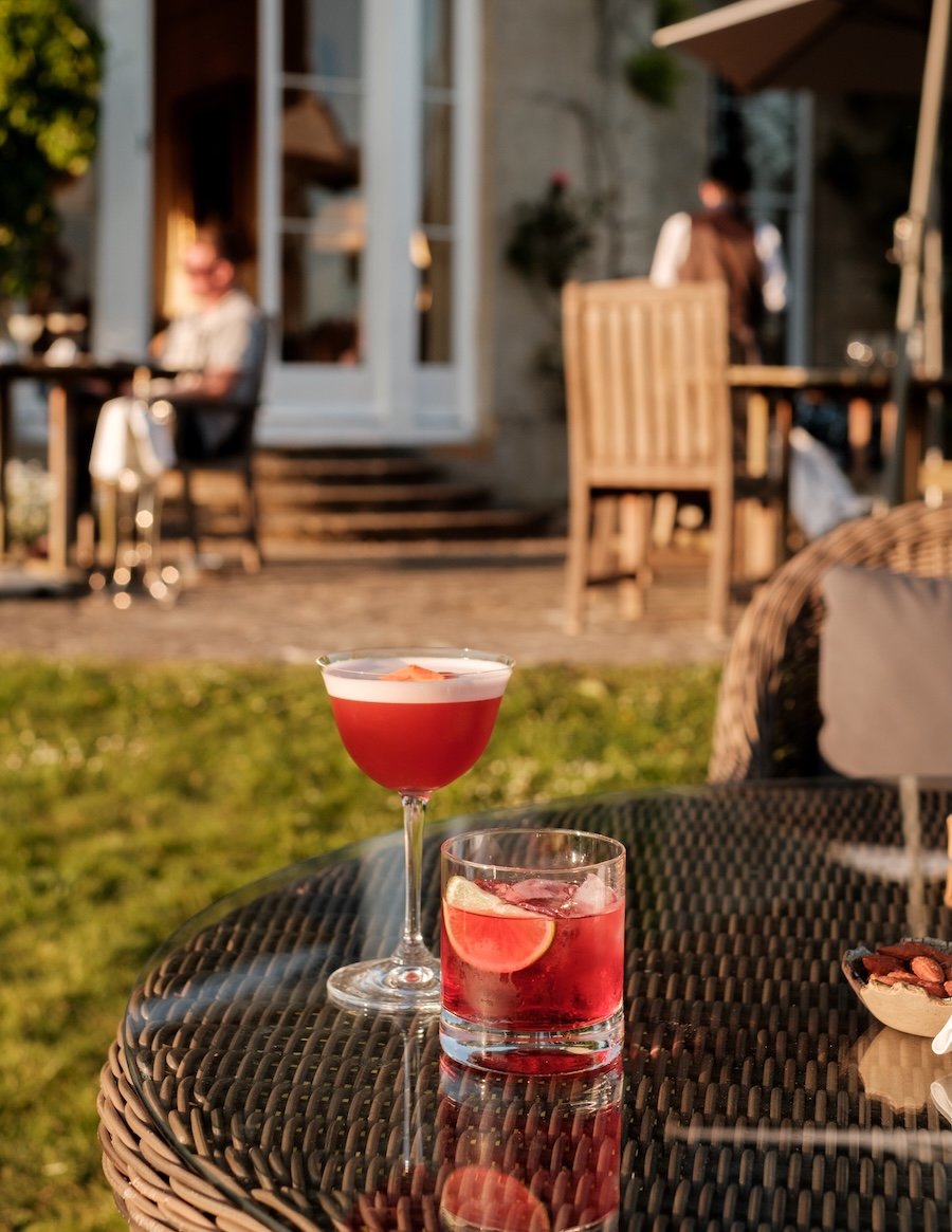 Two bright red cocktails rest on a sunny outdoor table