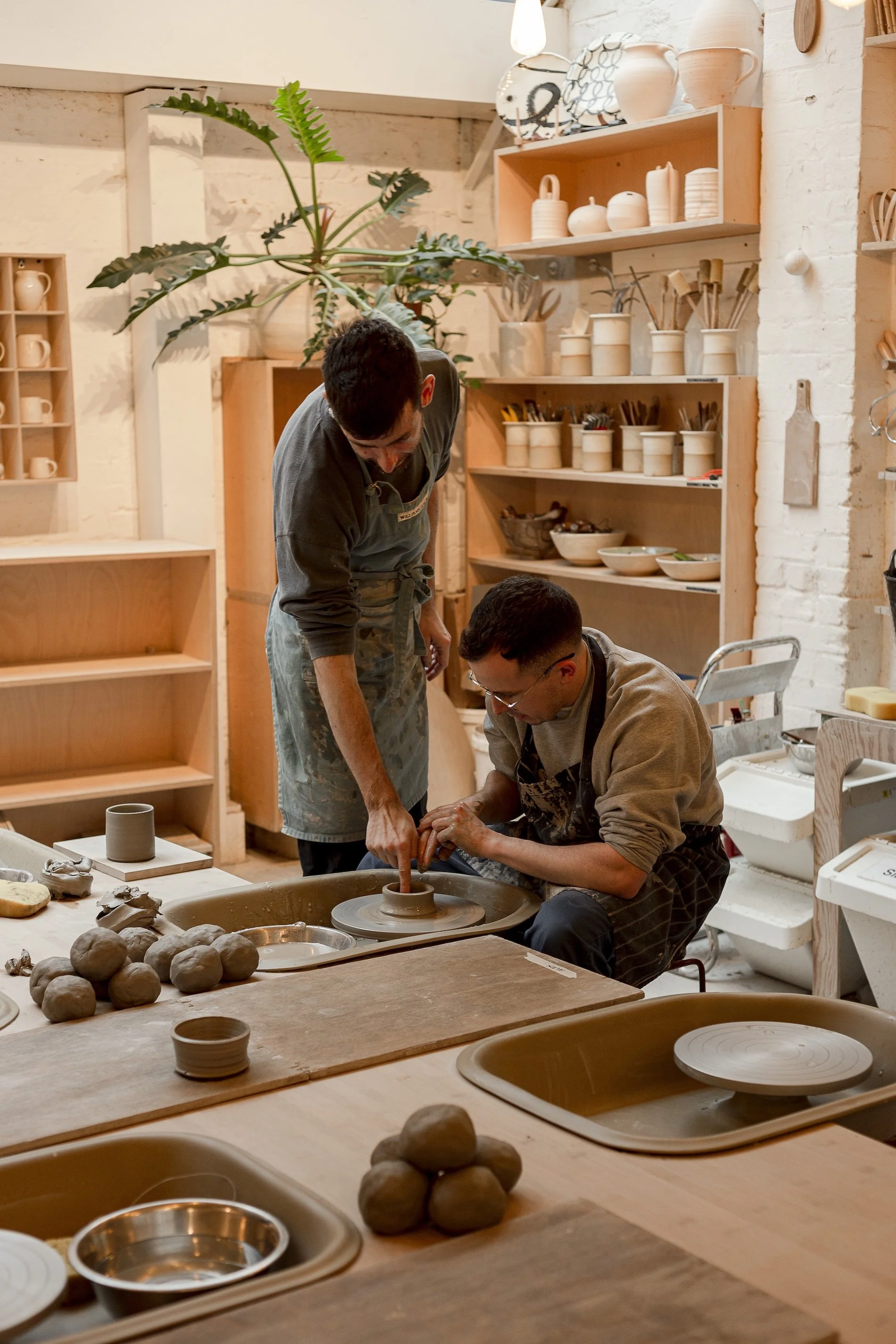 An instructor guides a student creating a clay vase in a pottery studio