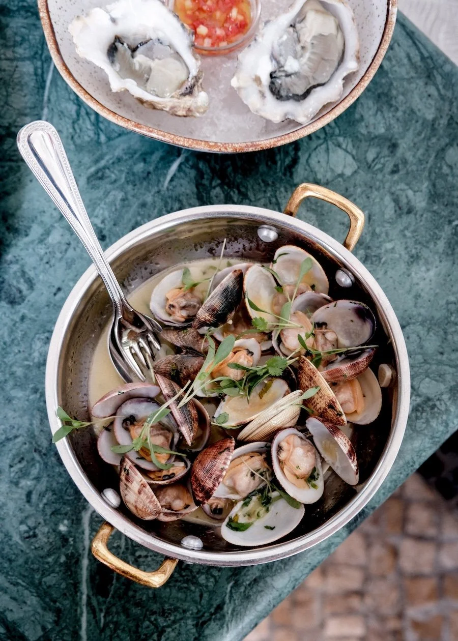 A plate of shucked oysters and a bowl of muscles rest on a marble table
