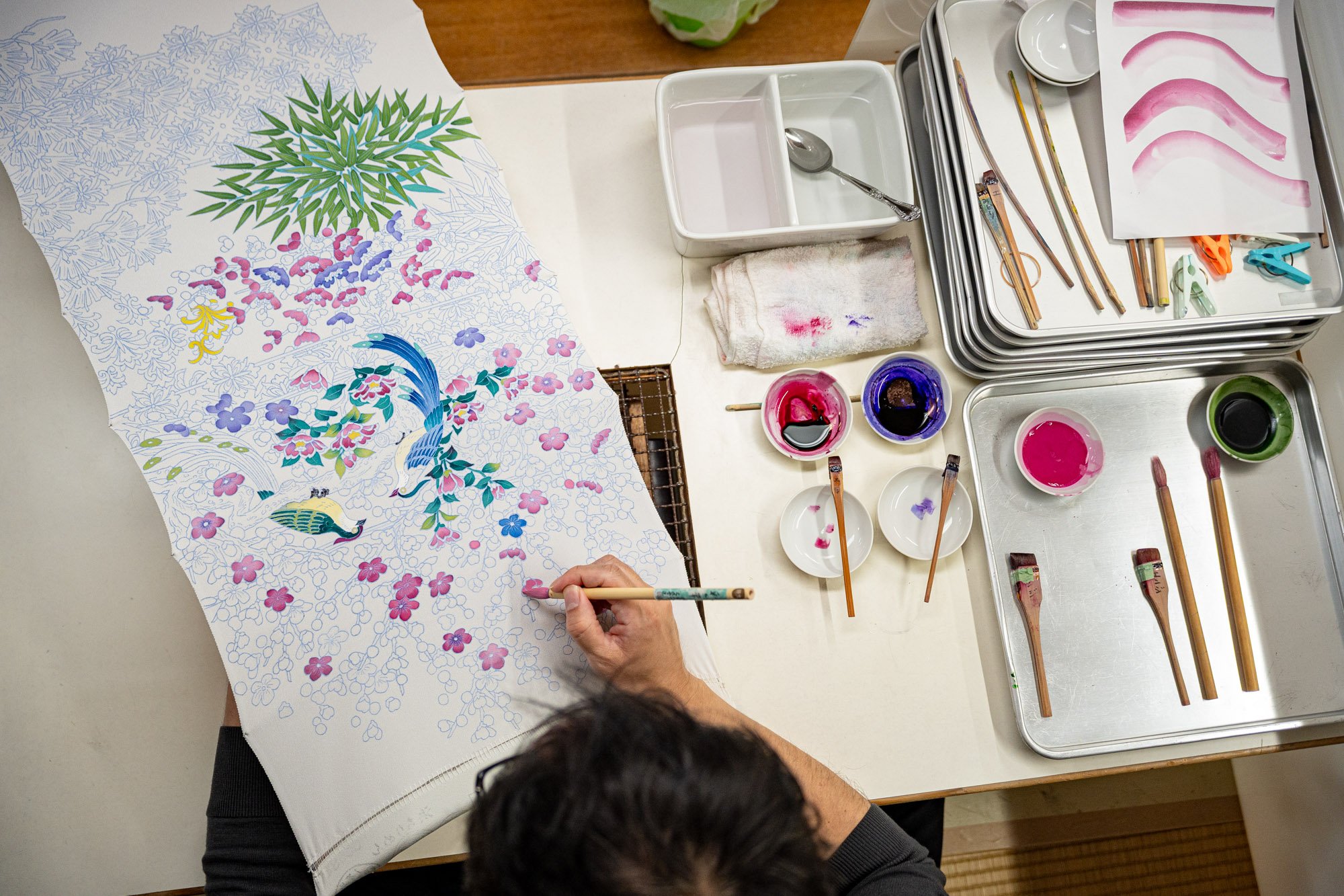 An artist hand paints blossoms onto a sheet of silk