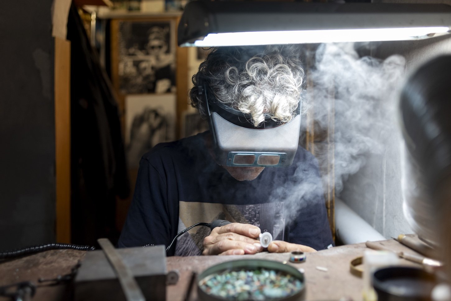 Smoke rises as an artis leans over the small pieces of colourful glass he is polishing