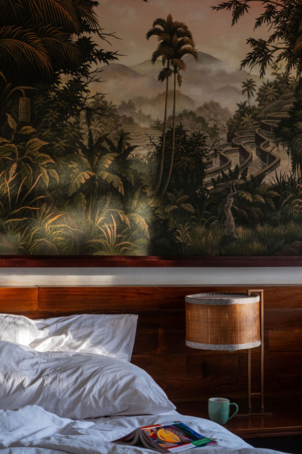 A closeup of a book and hotel bed, backdropped by wallpaper depicting a forest scene in Adiwana Suweta Resort, Bali