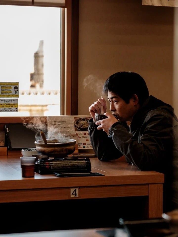 A man eats a steaming bowl of fish soup by the window at Himi Fishing Port, Japan
