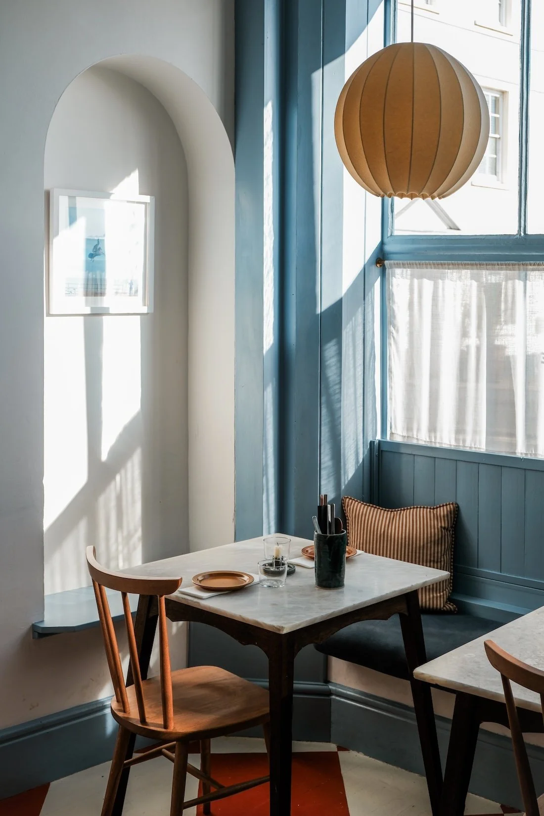 A small marble table stand in a ray on sunlight streaming in through a huge, blue-framed window