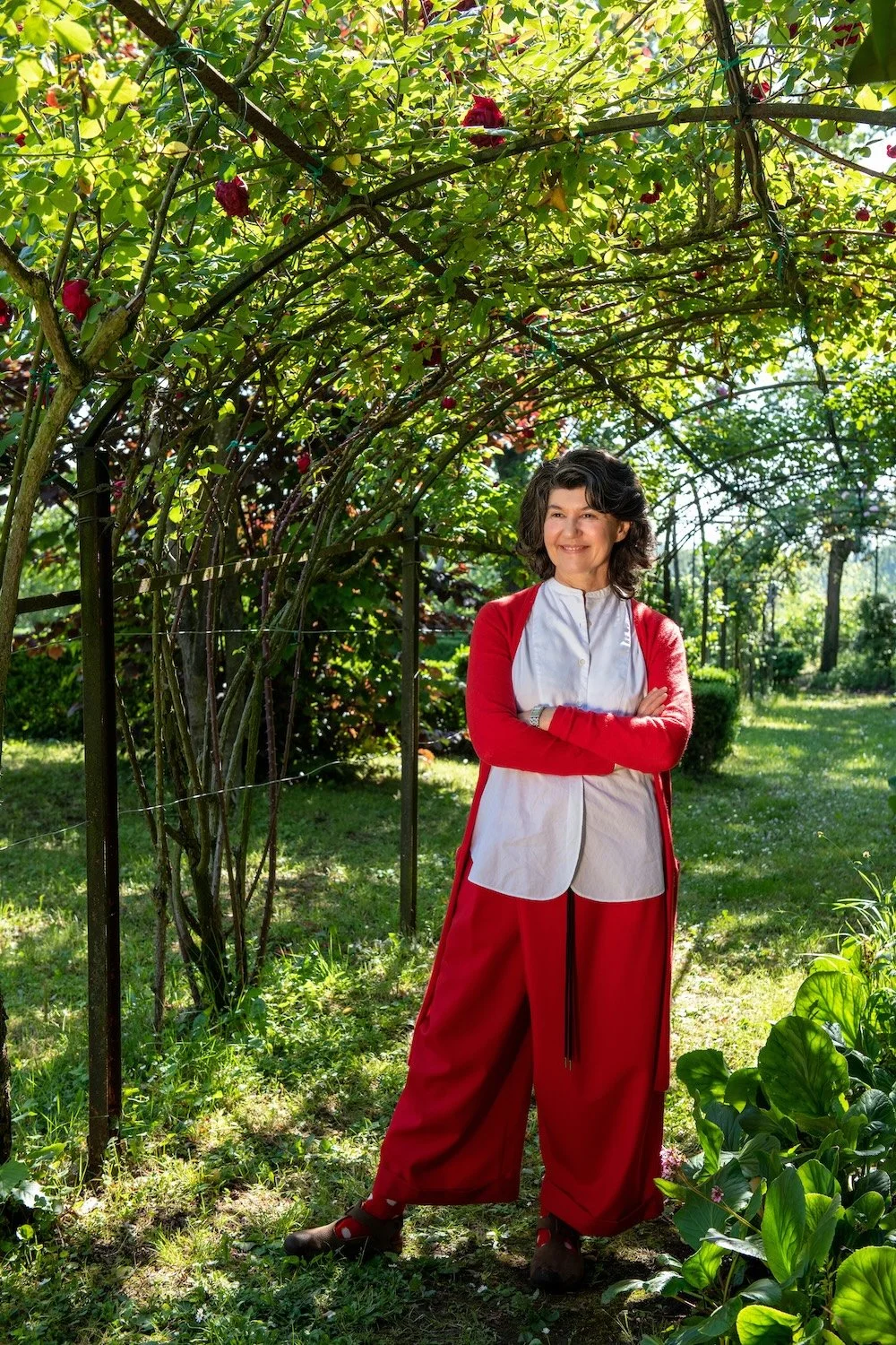 A woman dressed in red stands below a tunnel of red roses