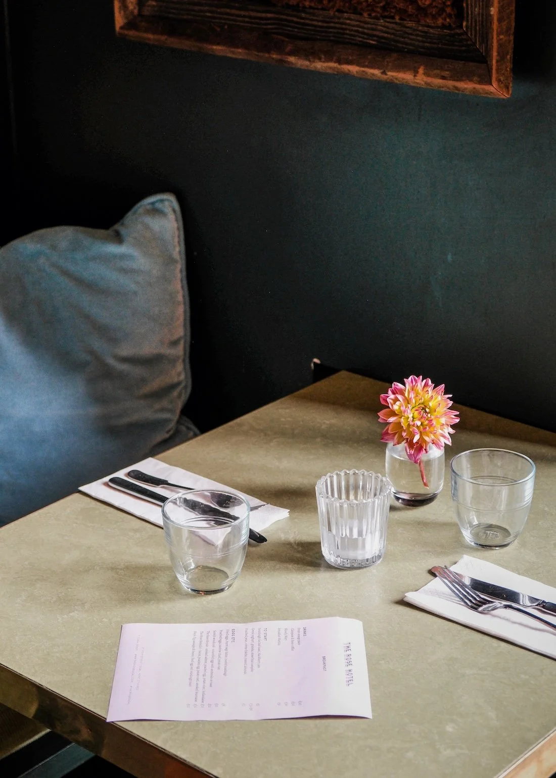 A olive-hued marble table, with a menu and single pink flower, backdropped by a dark blue wall at The Rose, Deal