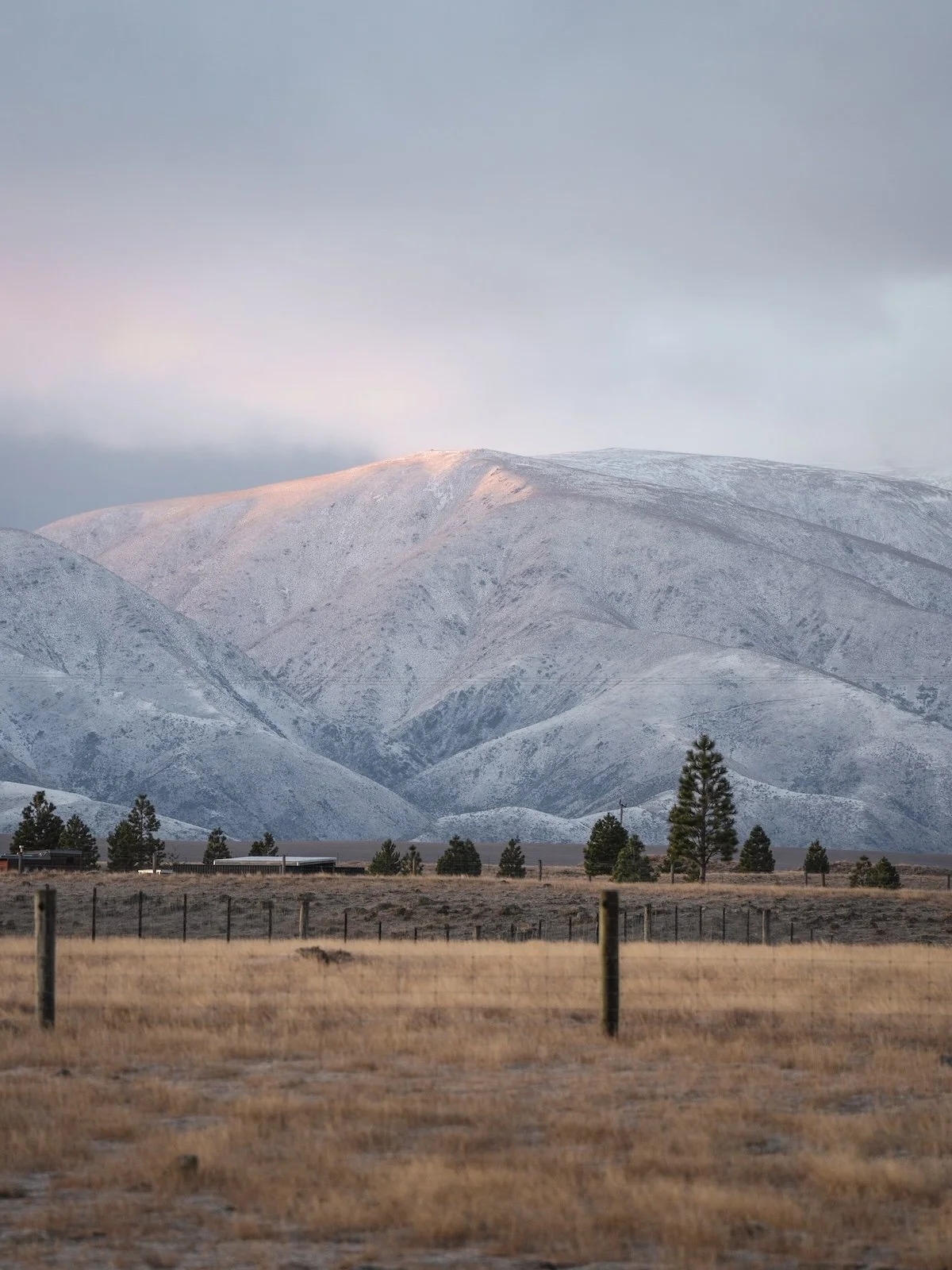 A snowy hill rises above farmland at sunset.